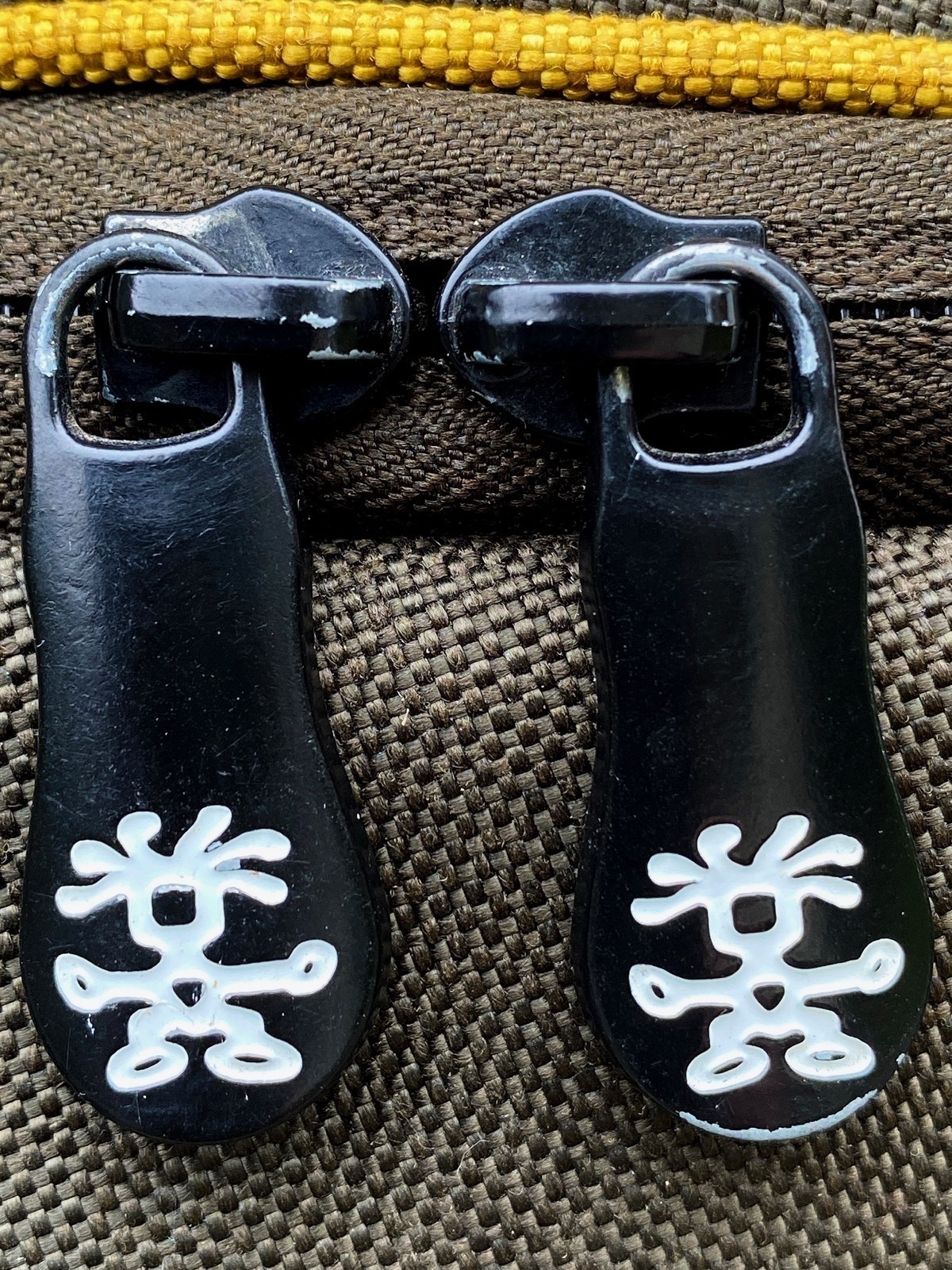 Close up of a zip and two black zip fasteners with white stick figures painted on them