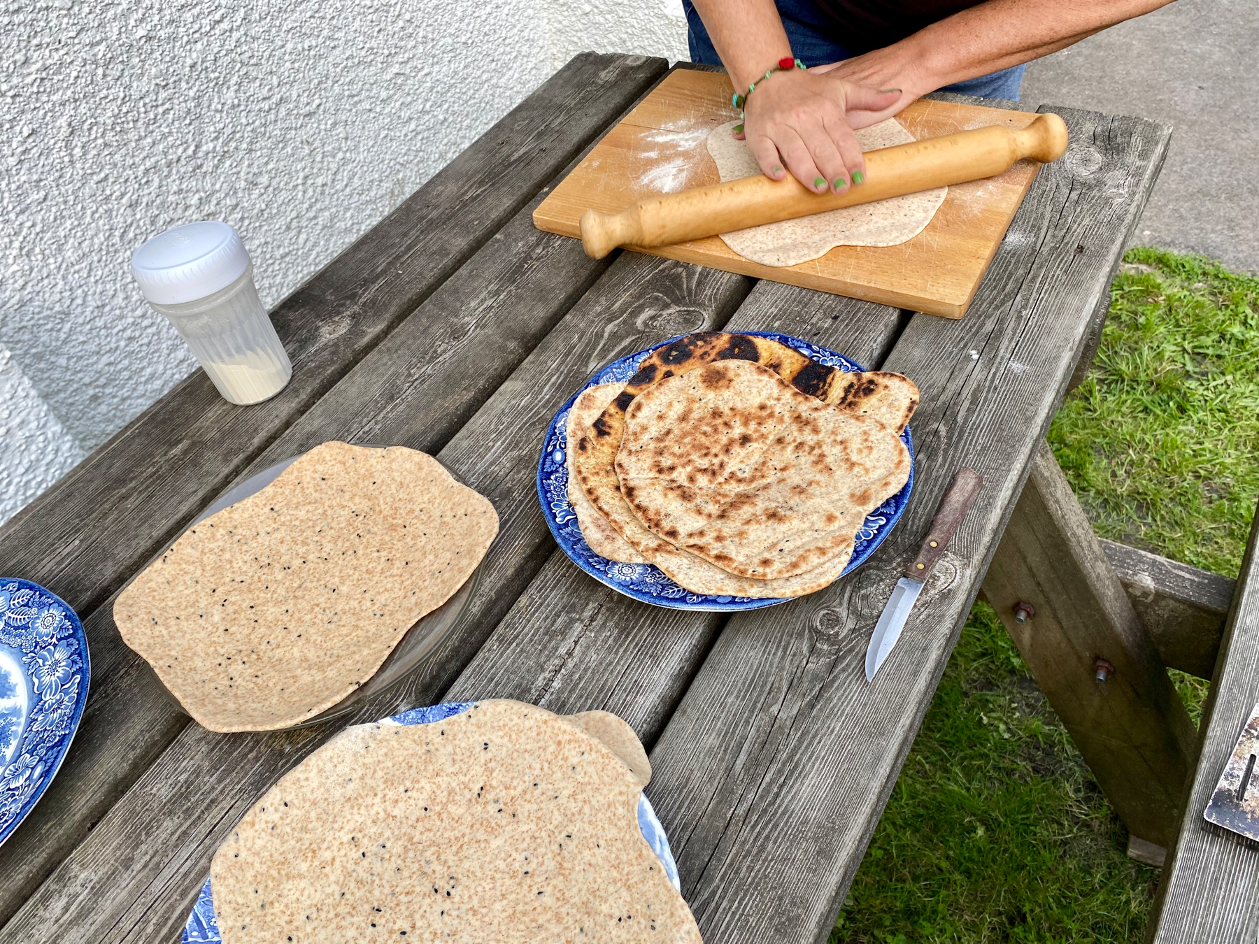 Table with plates containing cooked and uncooked flatbreads. One flatbread in process of being rolled out