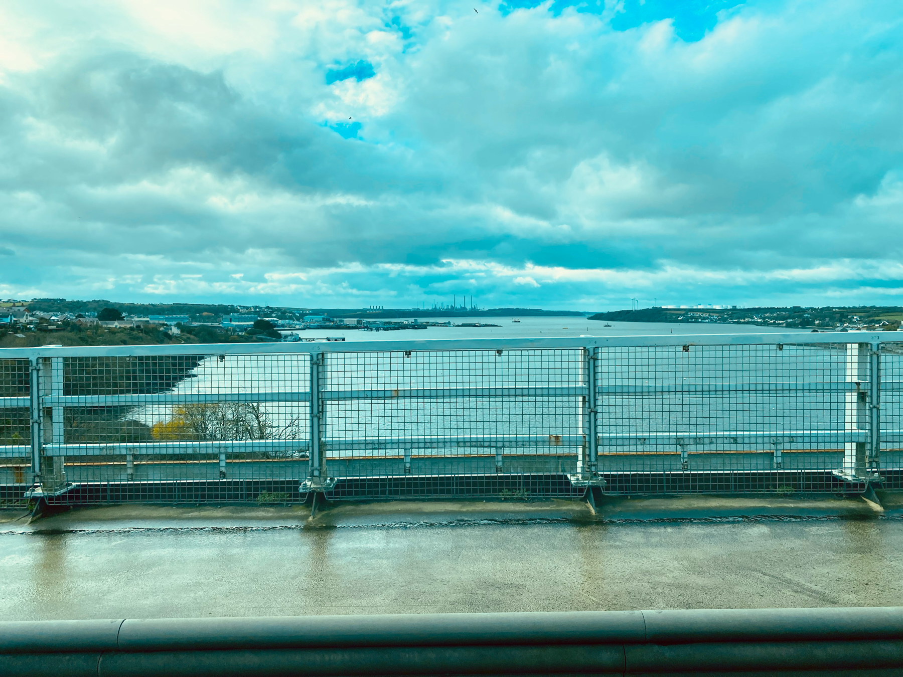 View from a bridge over wide river, white grid fence in foreground, cloudy sky