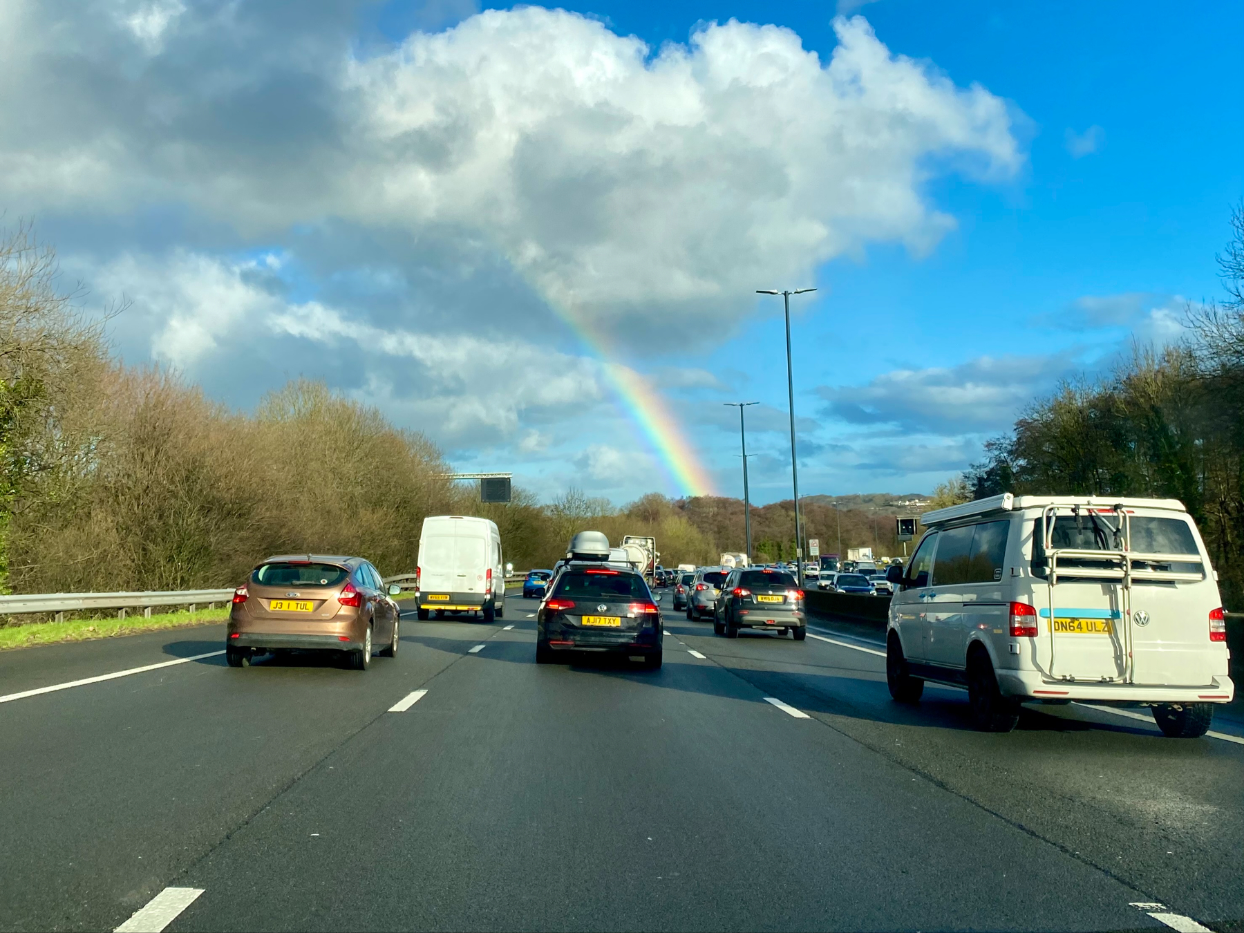 Motorway with queues of traffic but a rainbow in the sky