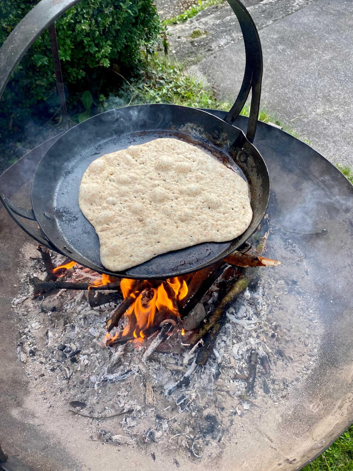 Close up of a flatbread cooking on a skillet over flames