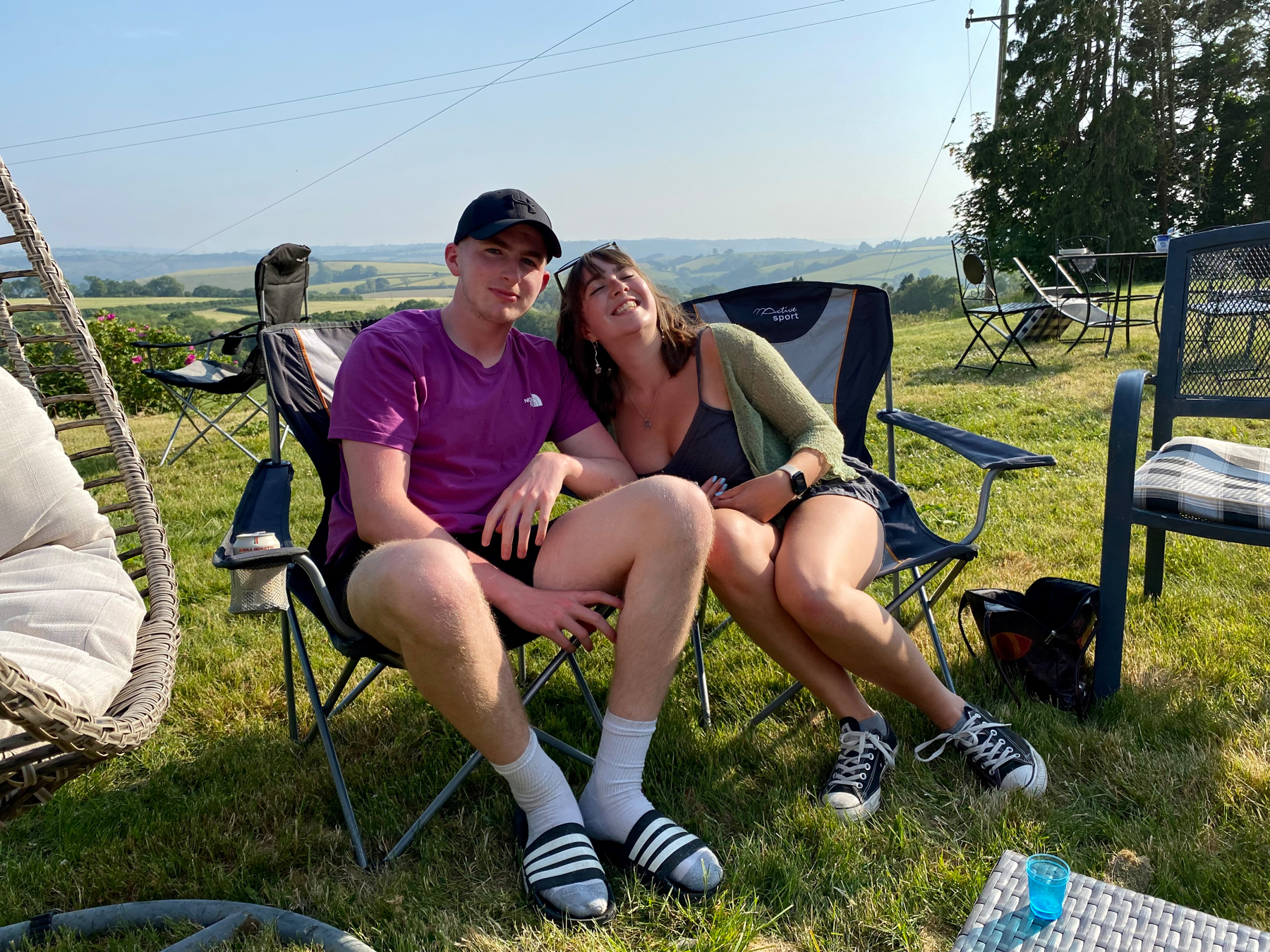 Young man and woman sitting next to each other on camping chairs, fields in background