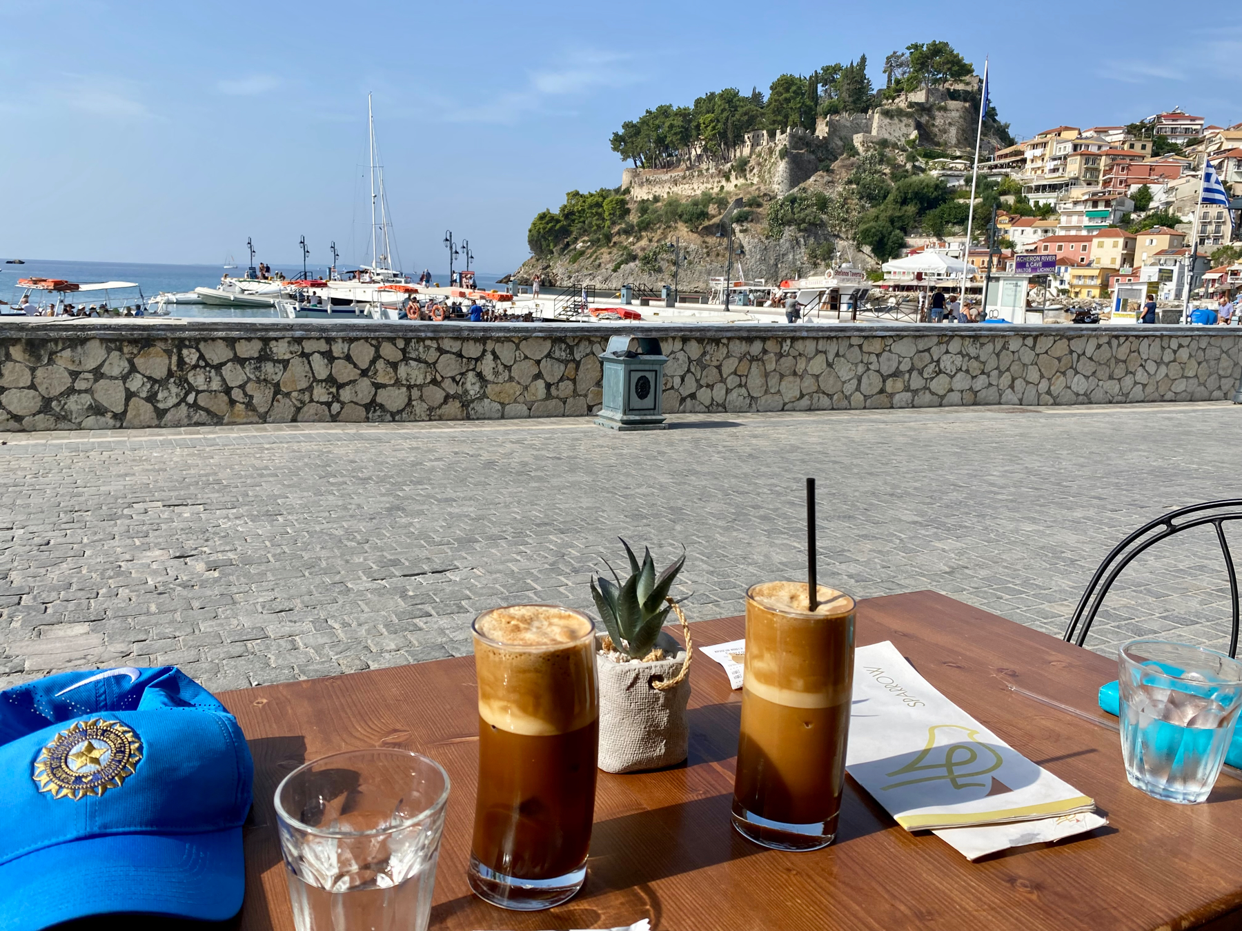 Two glasses of frothy iced coffee on a table overlooking boats in a harbour and castle on a hill