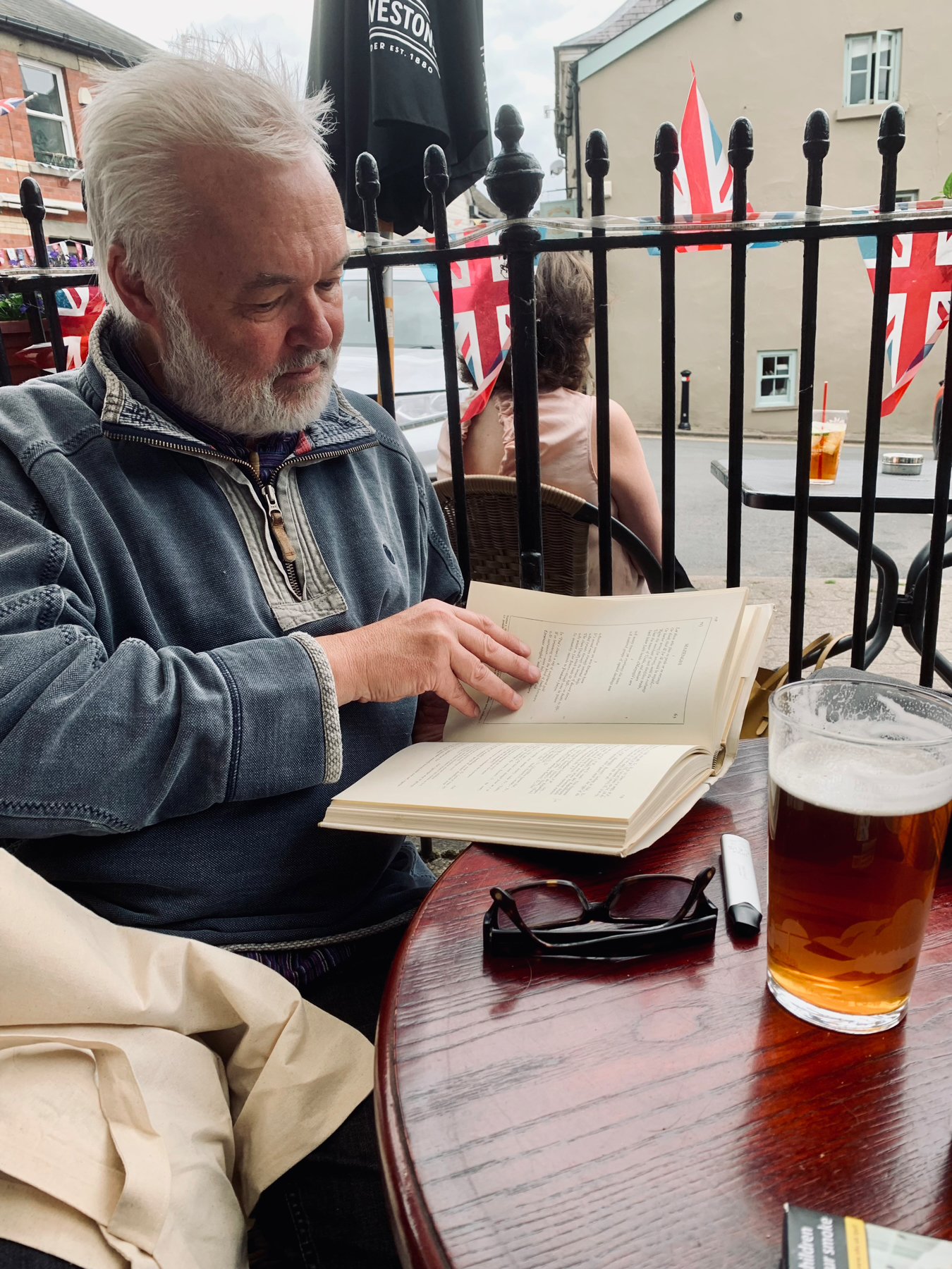 Man reading a book at an outdoor pub table, pint of beer in front of him