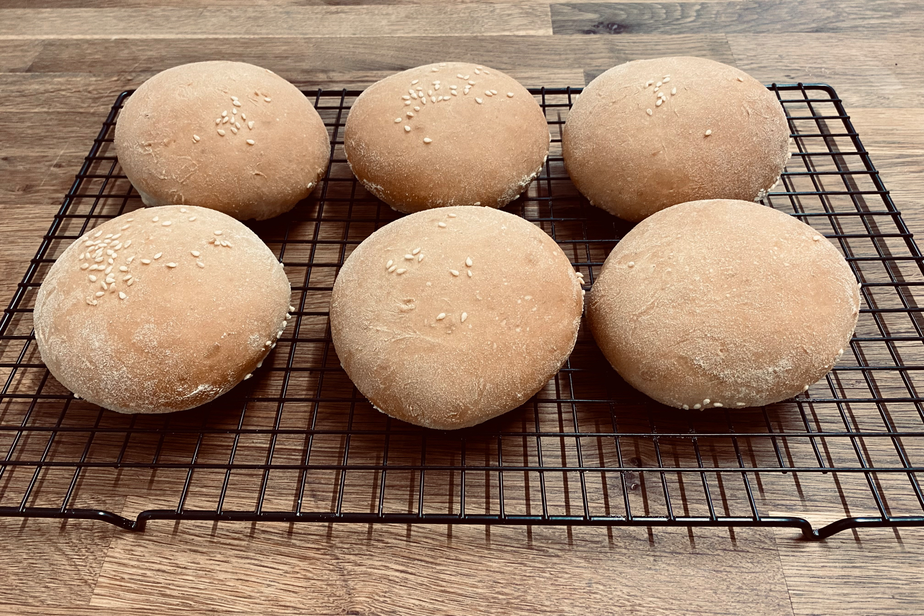 Six almost equally sized burger buns on a cooling rack
