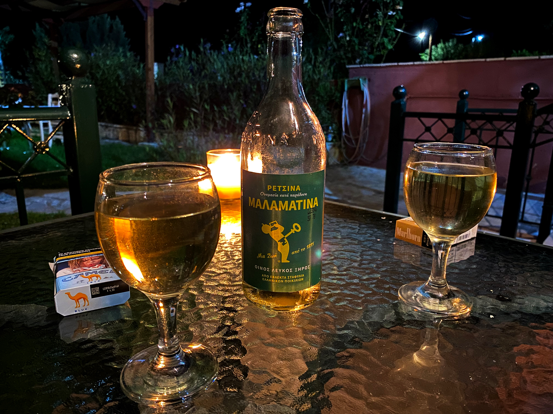 Two glasses of white wine and a bottle on a glass table illuminated by a candle behind them