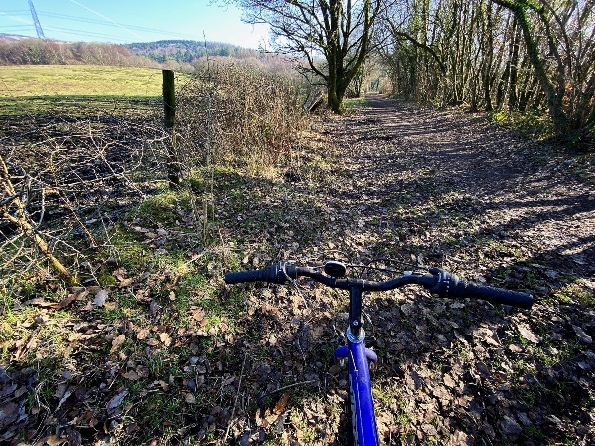 Bicycle handlebars in foreground, bridleway leading off into distance, fields and blue sky in background