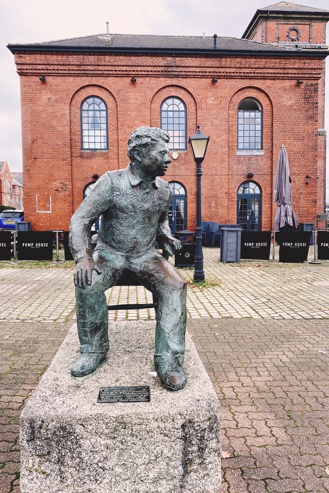 Statue of a seated man on a stone block in front of a red brick building