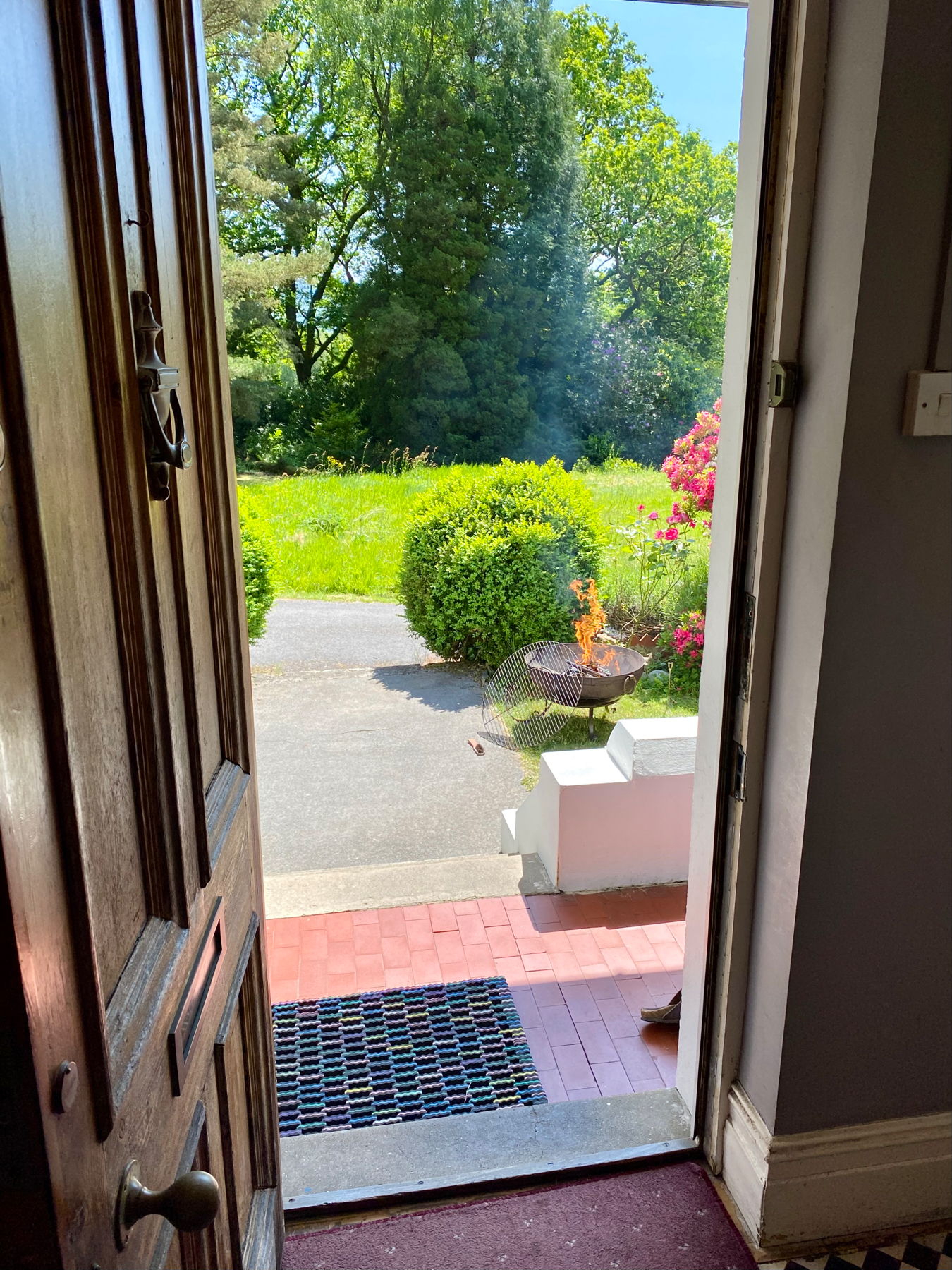 View from doorway of house looking into garden with a blazing metal fire pit and barbecue grill