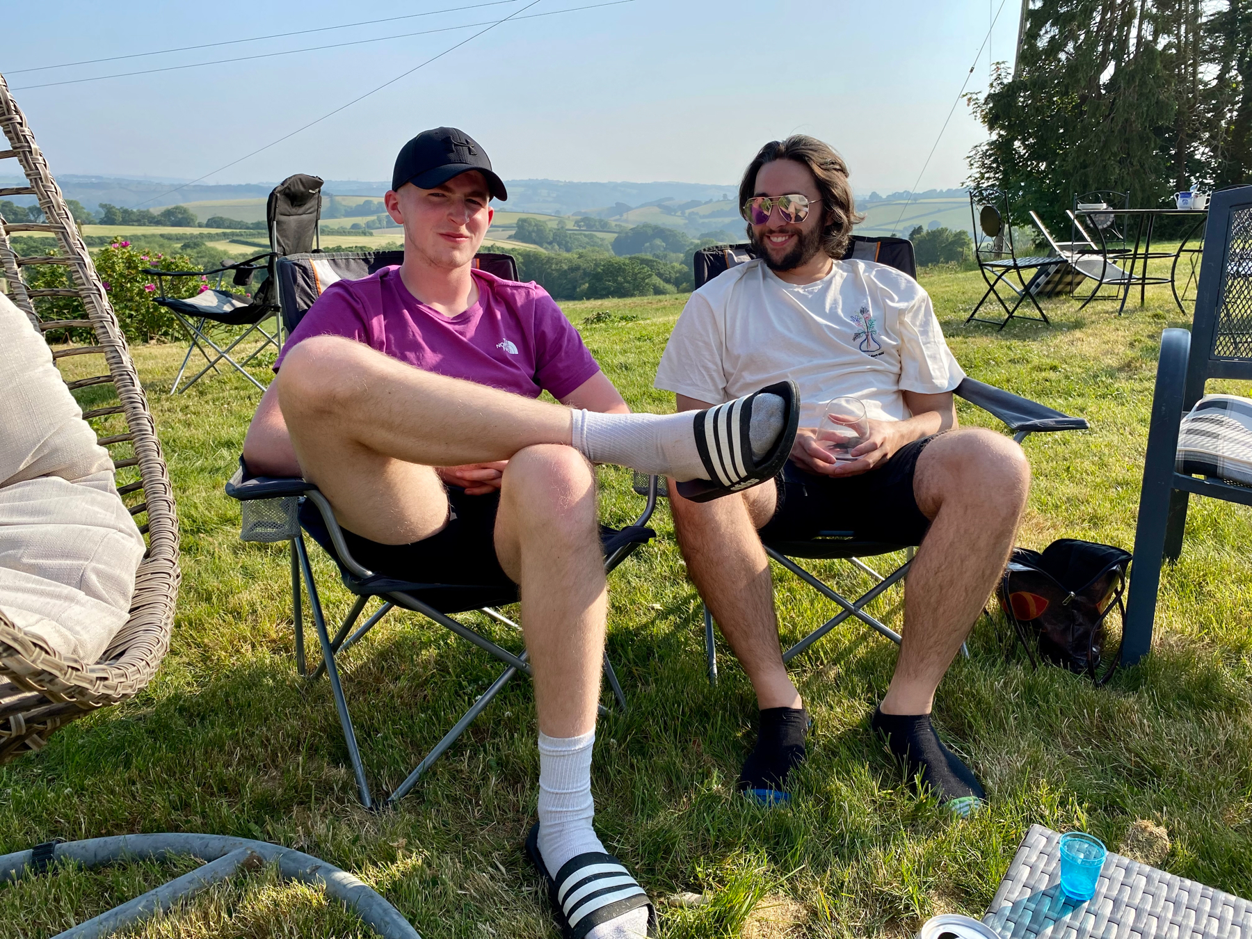 Two young men on camping chairs, fields in background