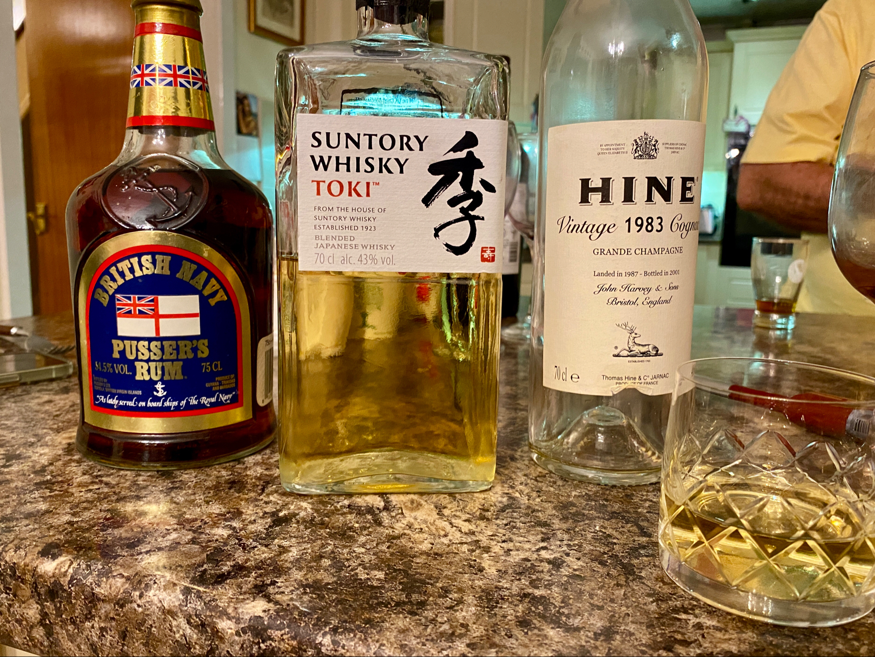 Three bottles of spirits in a row - rum, whisky and brandy - next to a glass of whisky