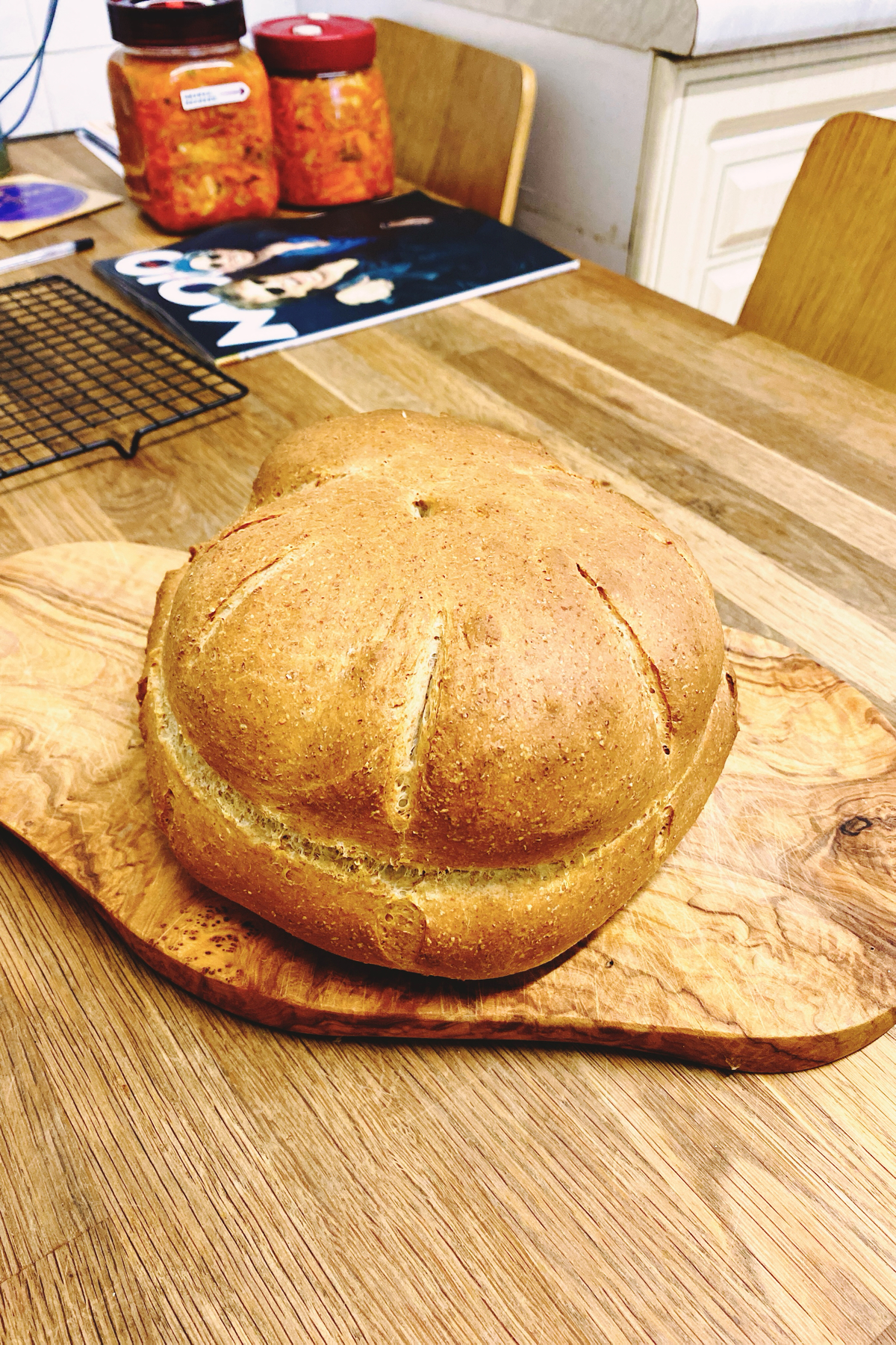Round, brown crusted loaf of bread on a wooden chopping board 