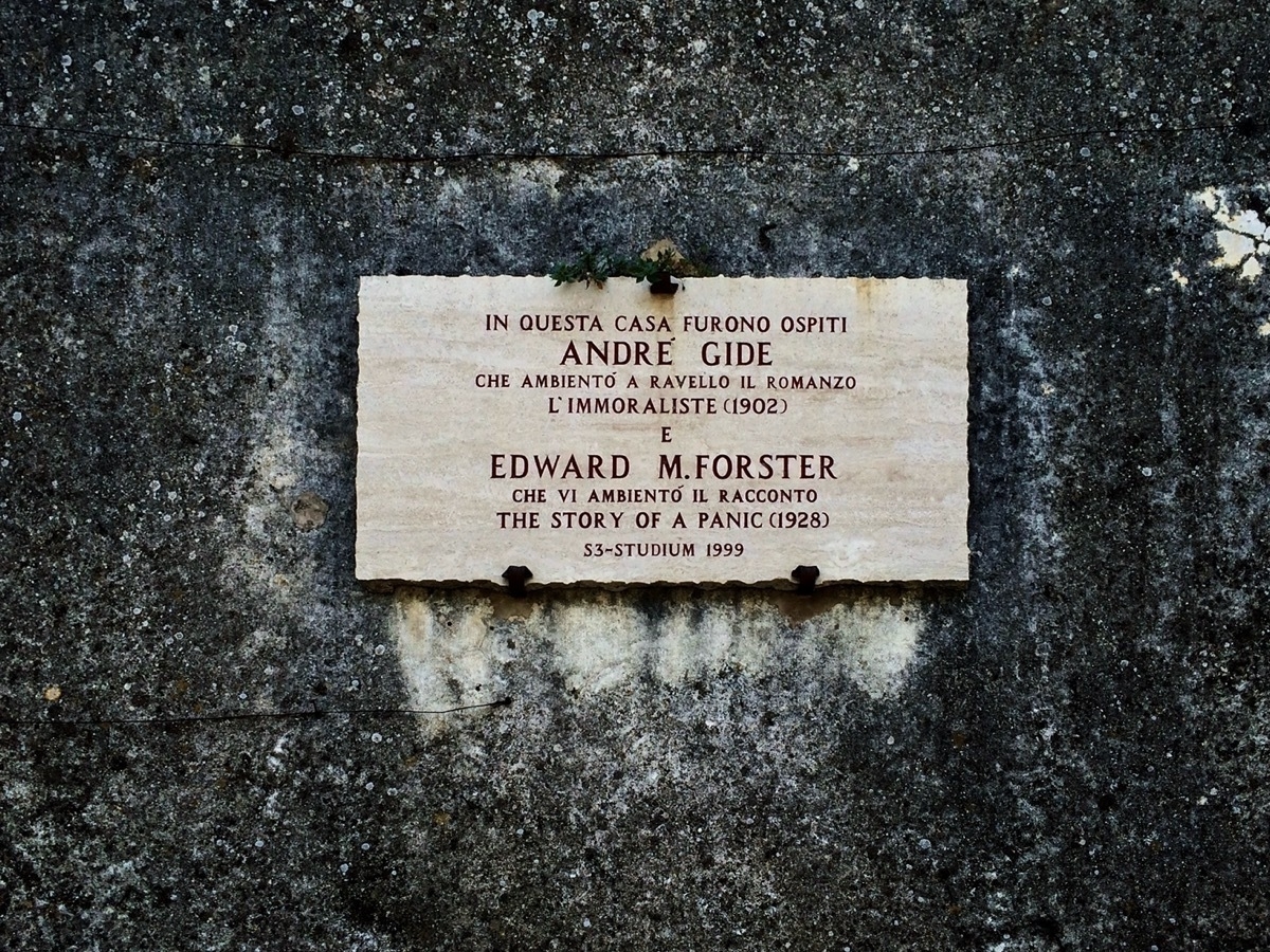 Patch of old, stained concrete wall with small white sign in the centre reading Edward M. Forster, The Story of a Panic, 1928