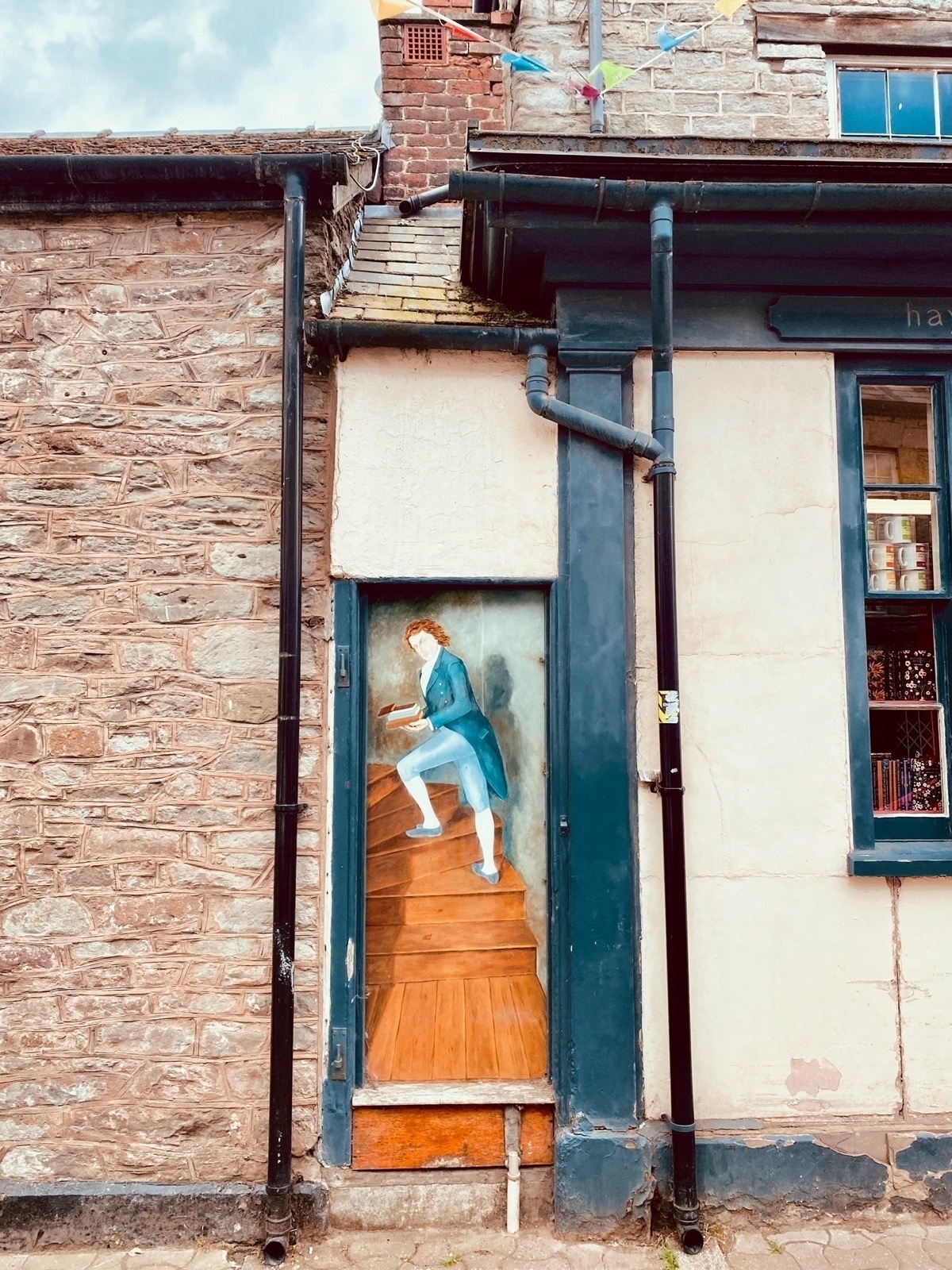 IImitation, painted doorway next to a shop showing a man in old-fashioned clothes holding a book and ascending a wooden staircase