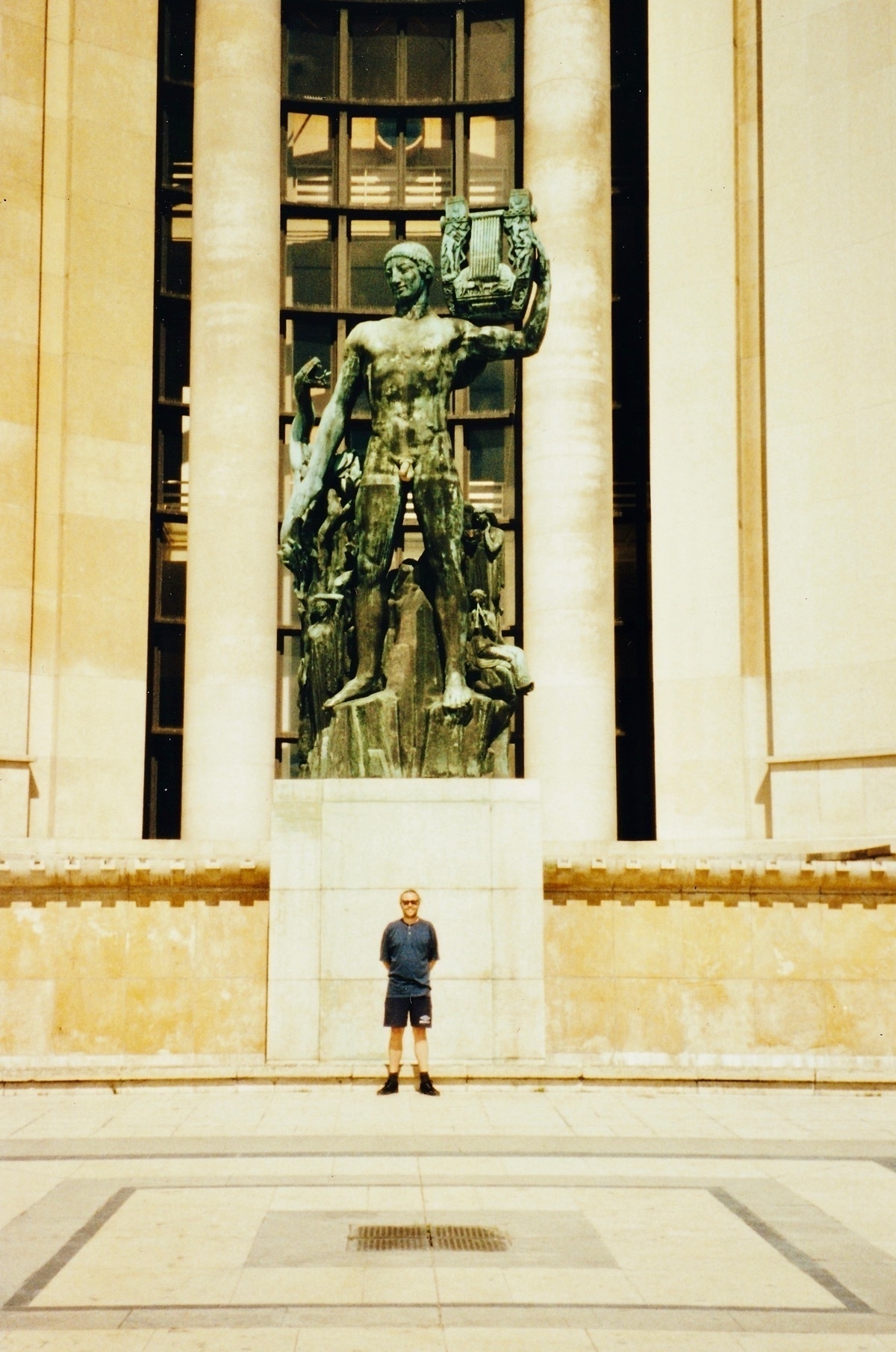 Man in shorts and t-shirt standing in front of a large bronze statue of Apollo