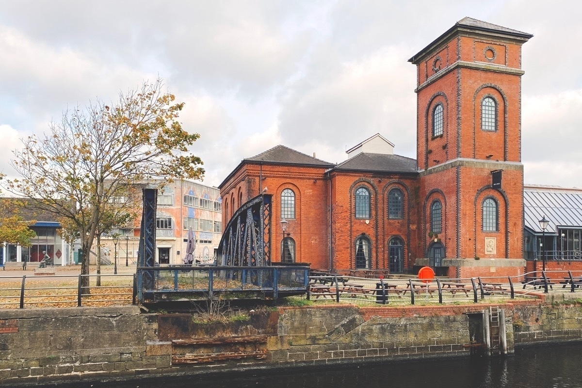 Red brick building with square tower alongside a dock and next to truncated section of an iron bridge