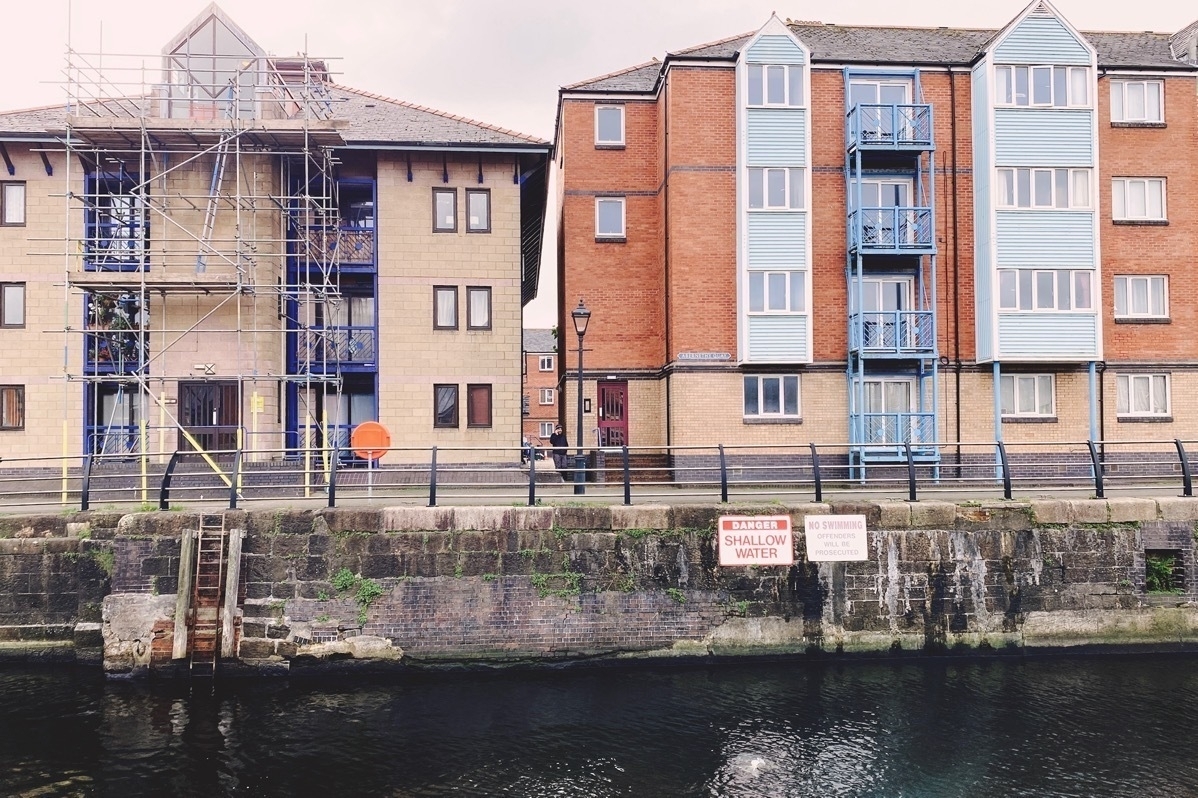 Modern multistorey buildings alongside an old dock. Sign warning of DANGER SHALLOW WATER