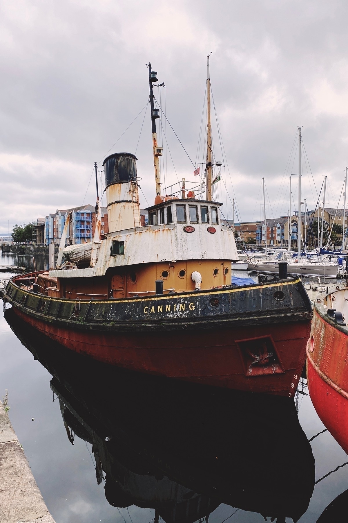 Old rusting black, white, red and yellow tugboat moored in a marina