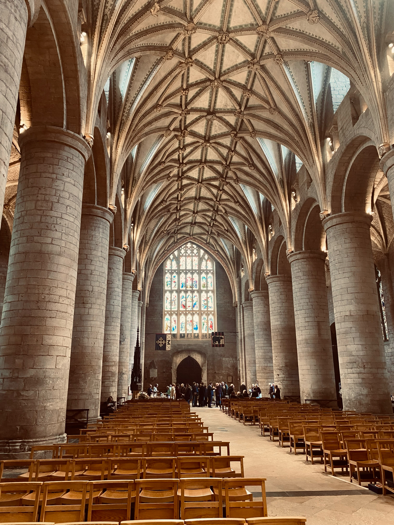 Interior of a Gothic cathedral showing vaulted ceilings, stained glass windows, stone columns, and rows of wooden chairs.