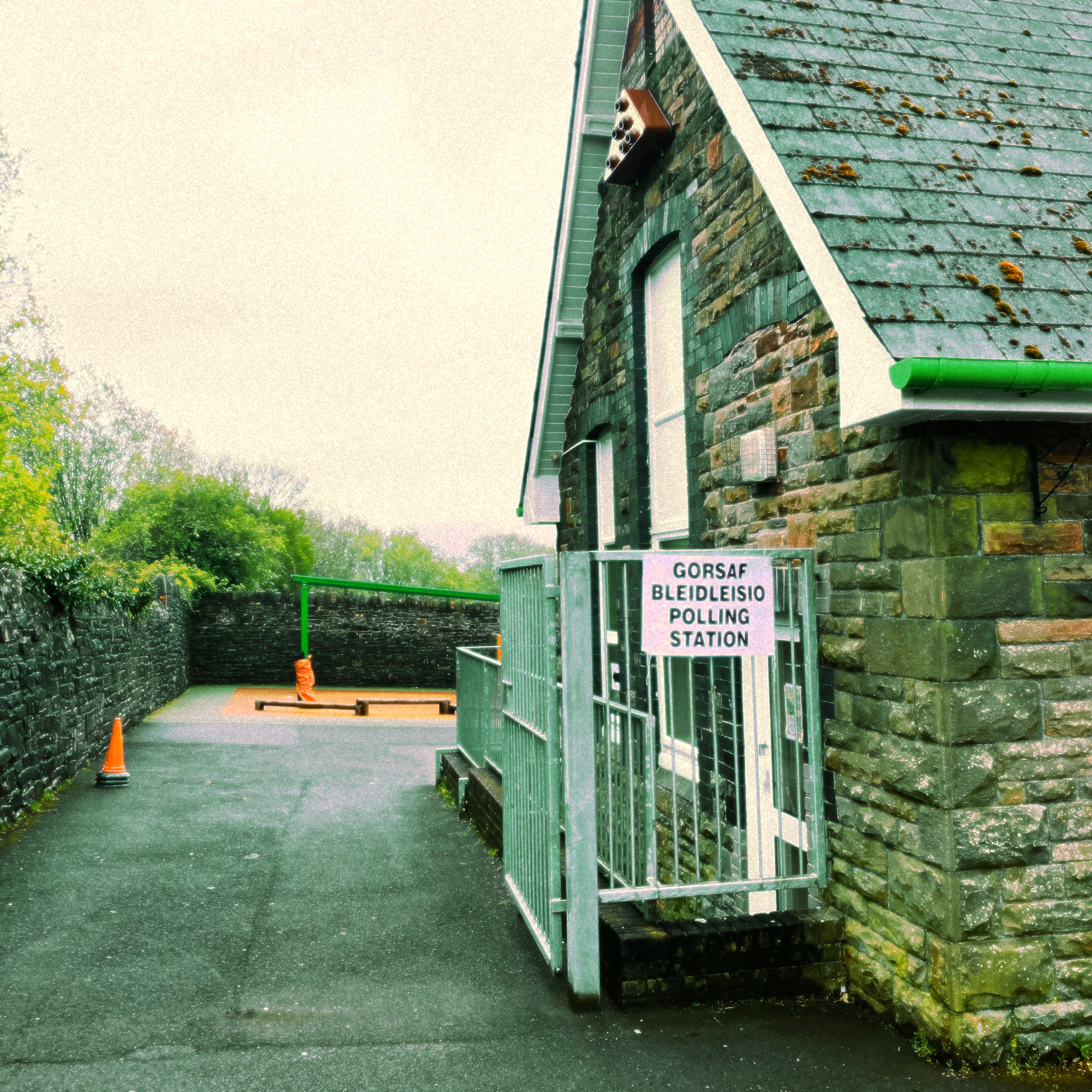 Old stone building, yard and walls with a Polling Station sign in Welsh and English pinned up on fencing outside