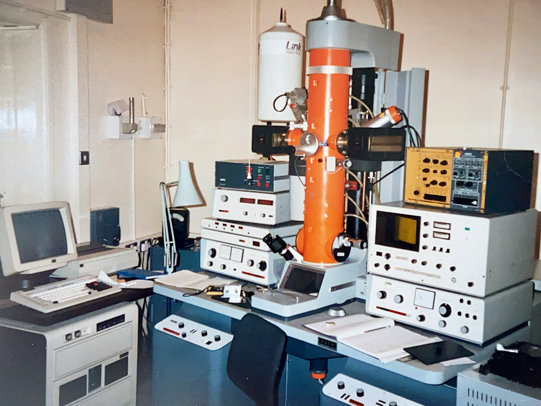 A laboratory setup with an old computer, various electronic measurement devices, and an electron microscope.