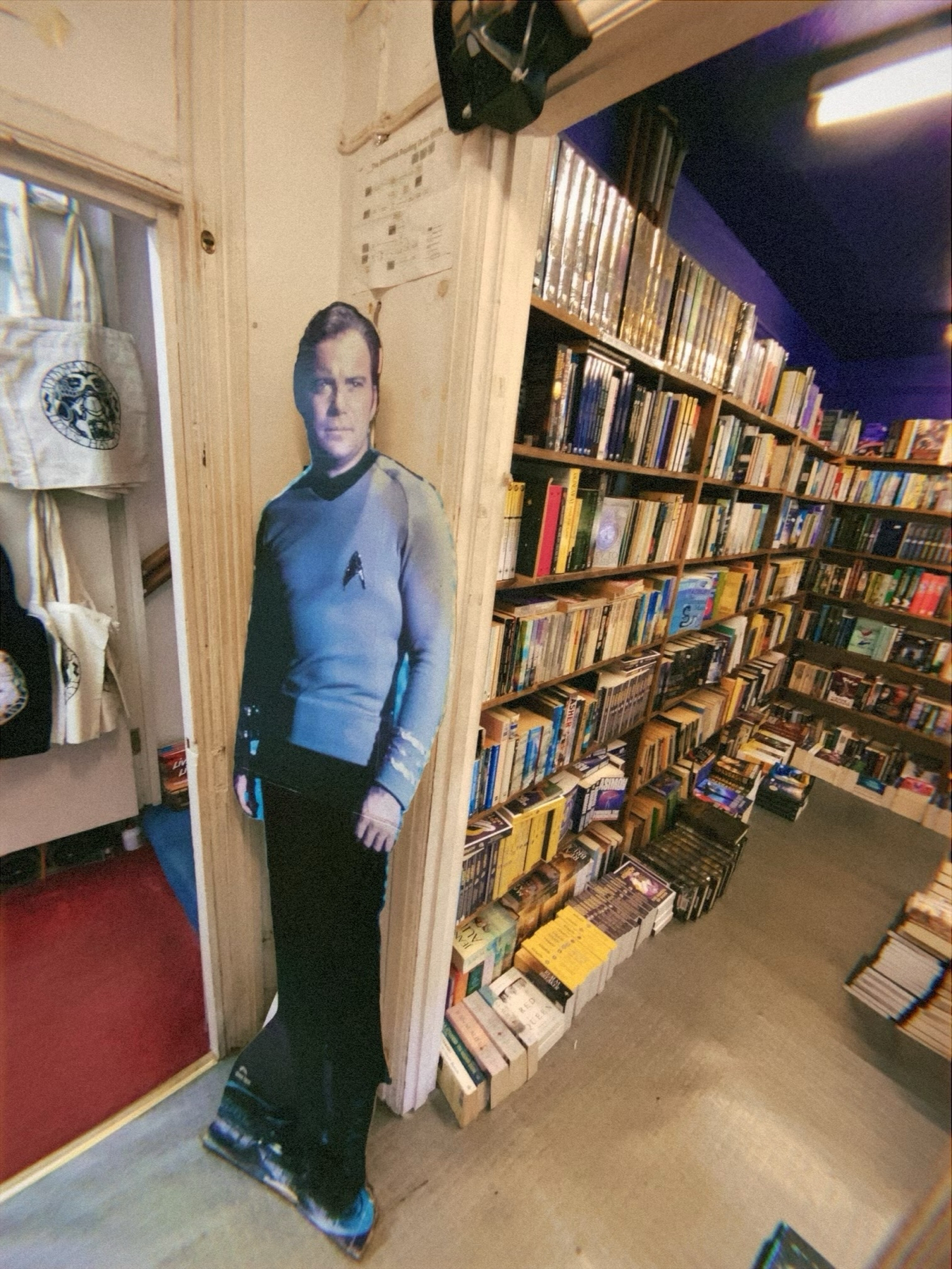 A life-size cardboard cutout of a Star Trek character stands at the entrance of a bookstore with rows of bookshelves filled with various books.