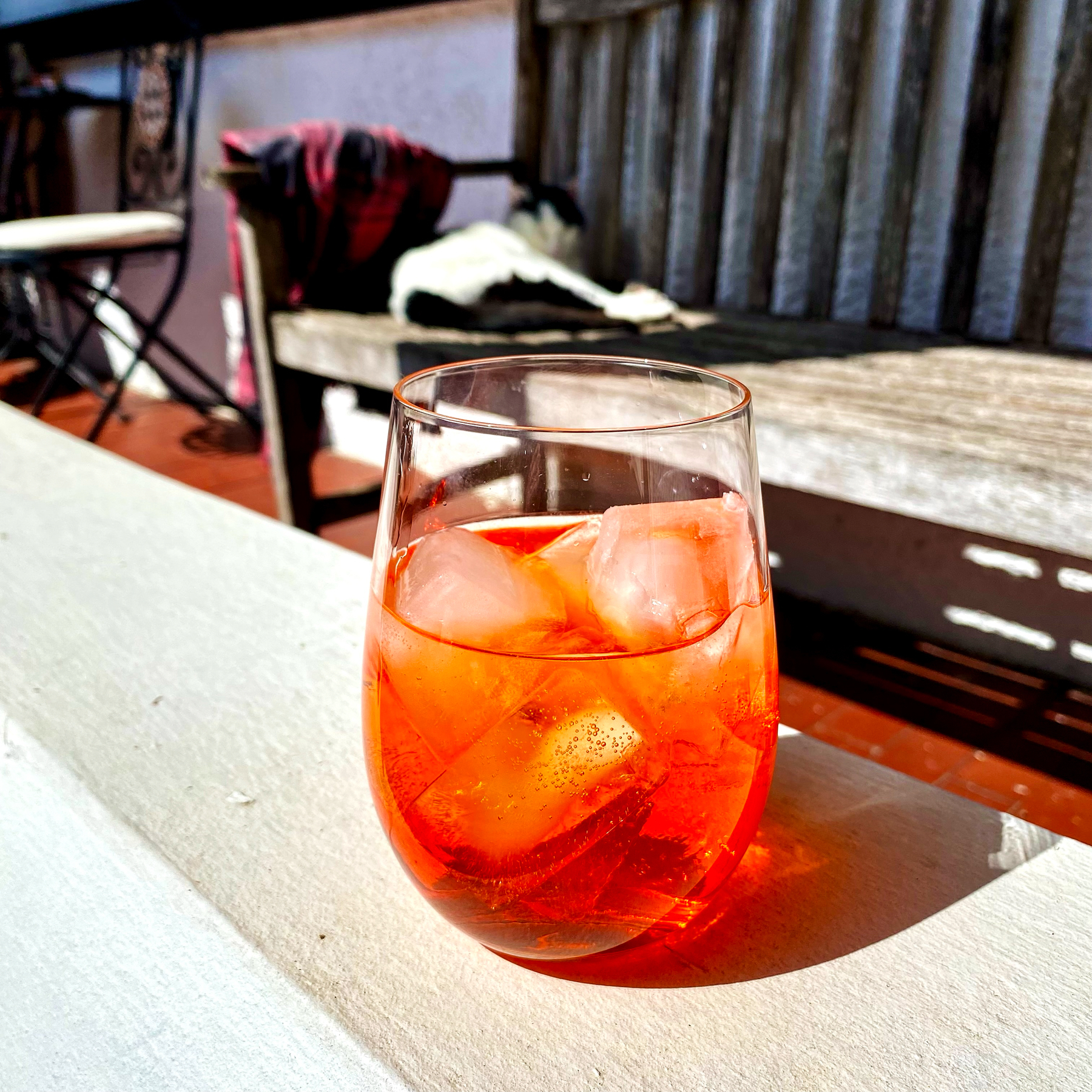 A glass of iced beverage on a sunny day, with a blurred background featuring outdoor seating.