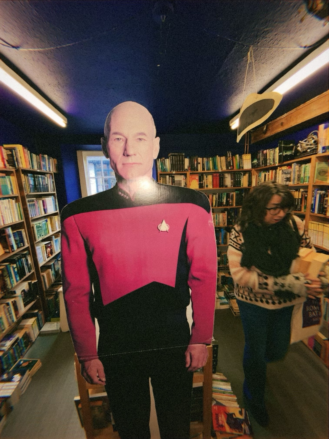 A cardboard cutout of a character in a red and black Starfleet uniform from Star Trek inside a bookstore with a woman carrying books walking in the background.