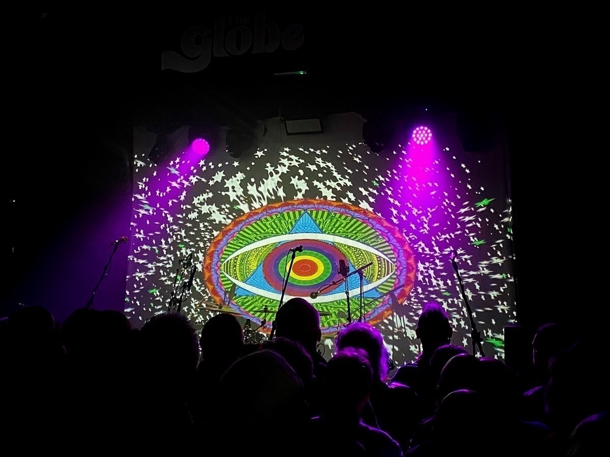 Concert scene with audience silhouettes in front of a stage with psychedelic eye projection and purple stage lights