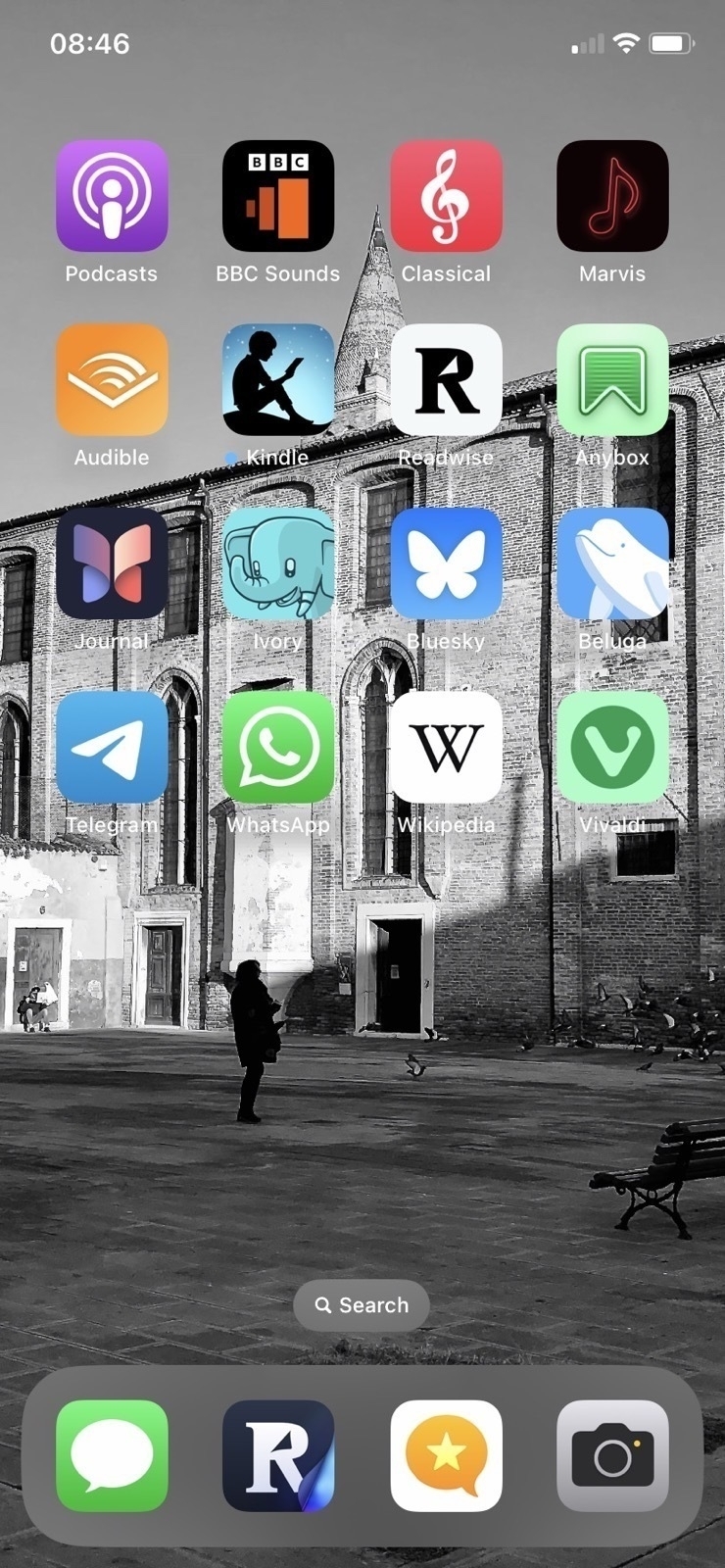 A smartphone screen displaying various app icons. The background is a black and white photo of a square with people and birds.