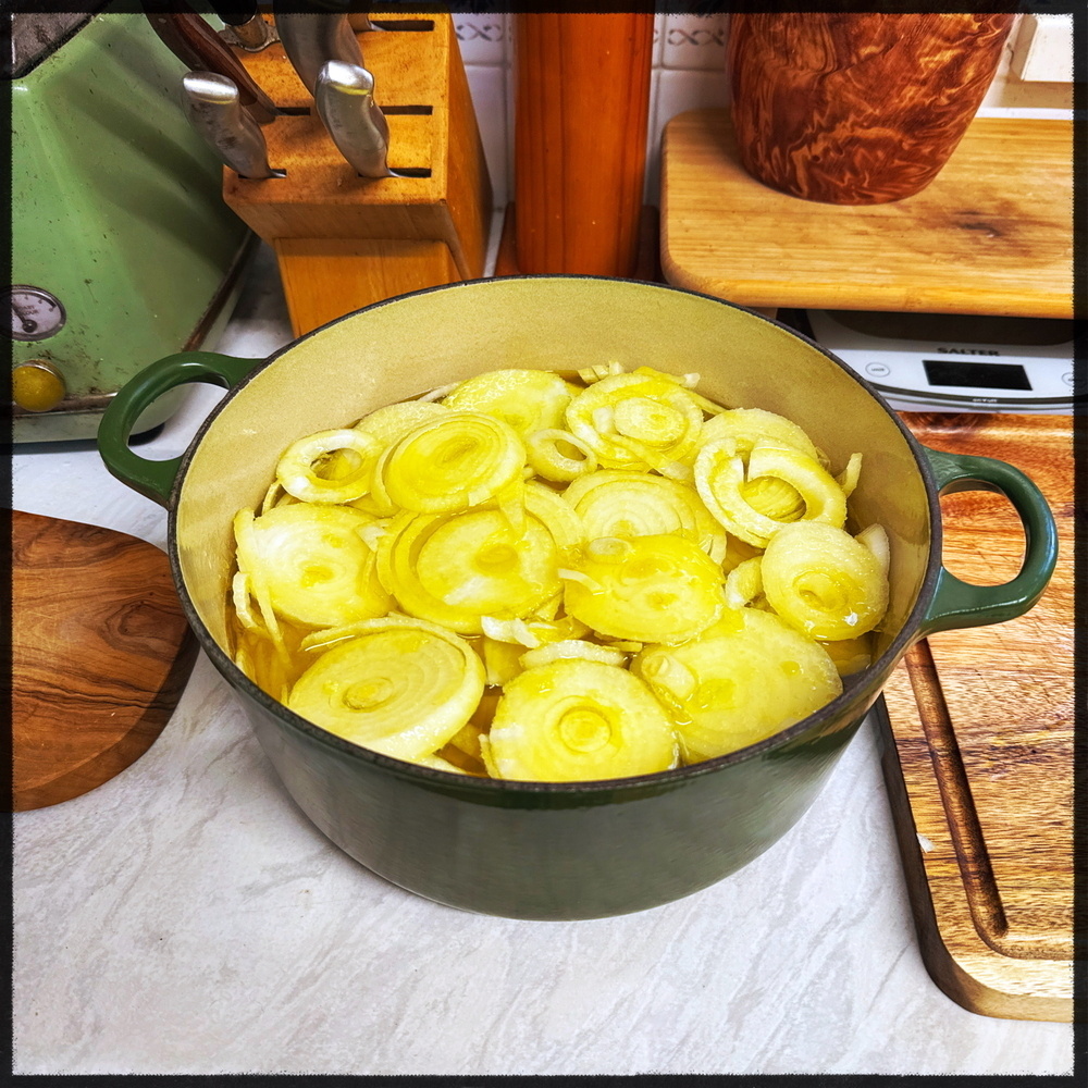 A green pot filled with sliced onions is placed on a kitchen counter.