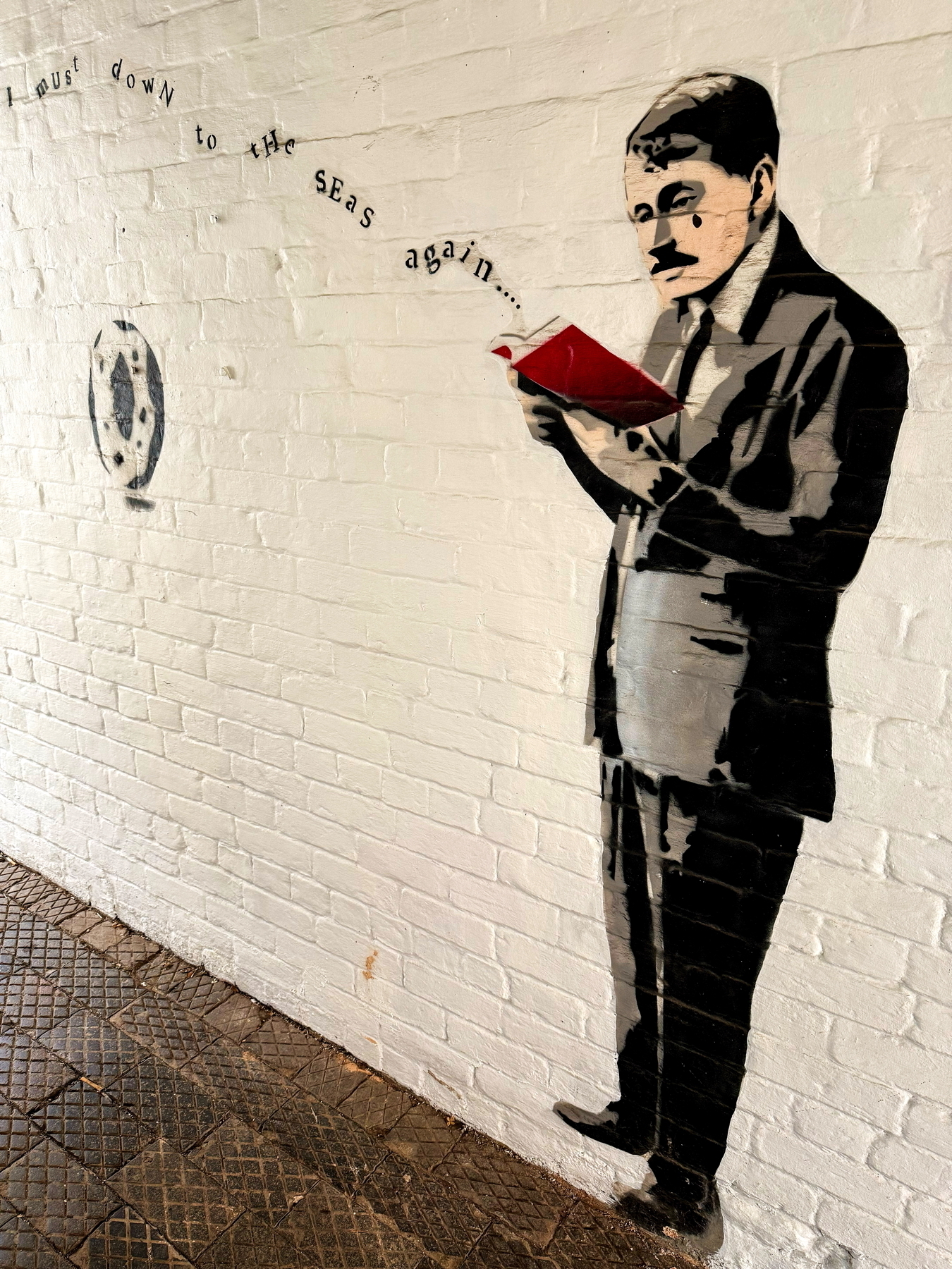 Auto-generated description: A mural on a brick wall depicts a man reading a red book with swirling text.