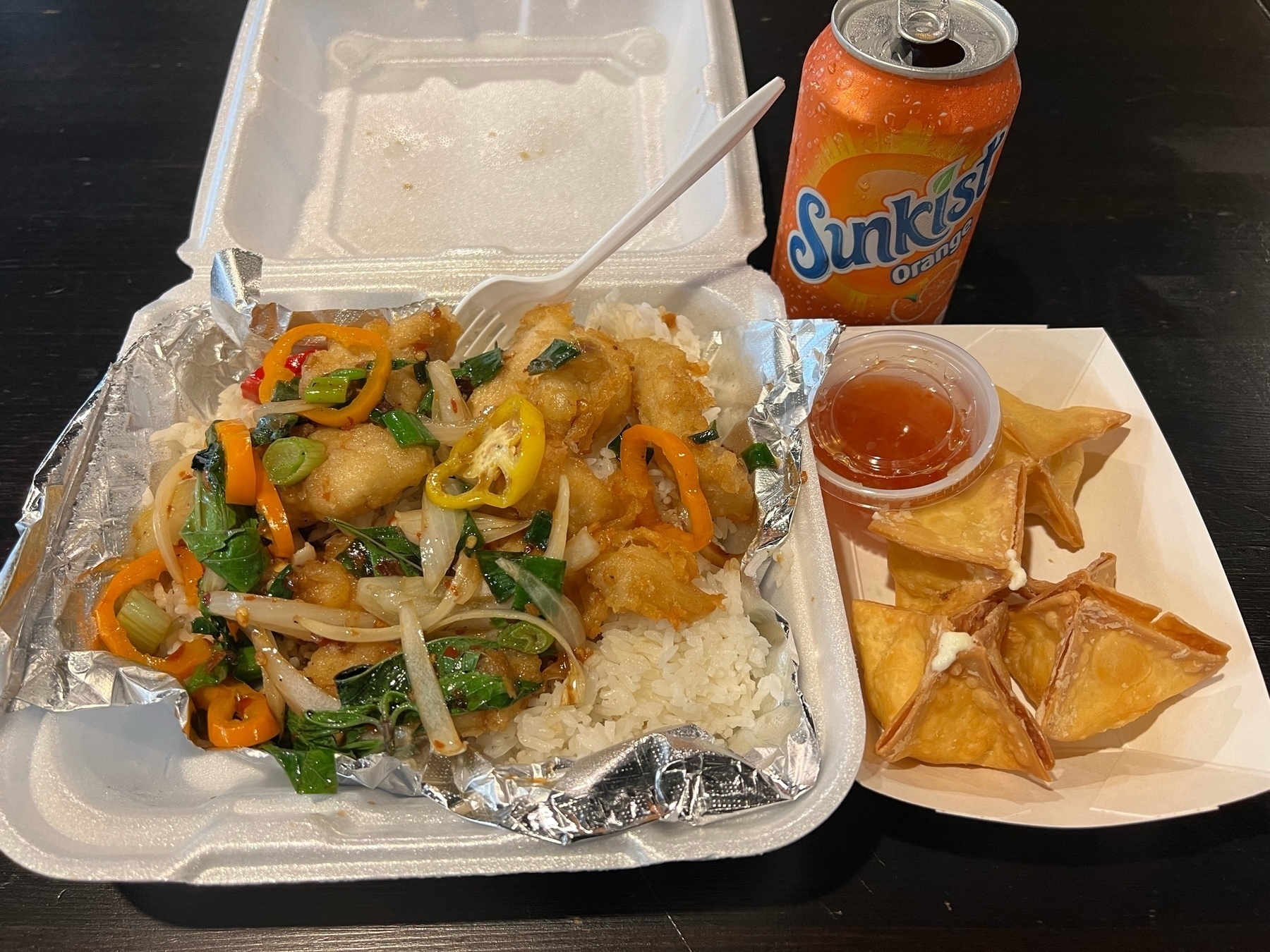 a table with a plate of crispy basil chicken, crab rangoon, and orange soda