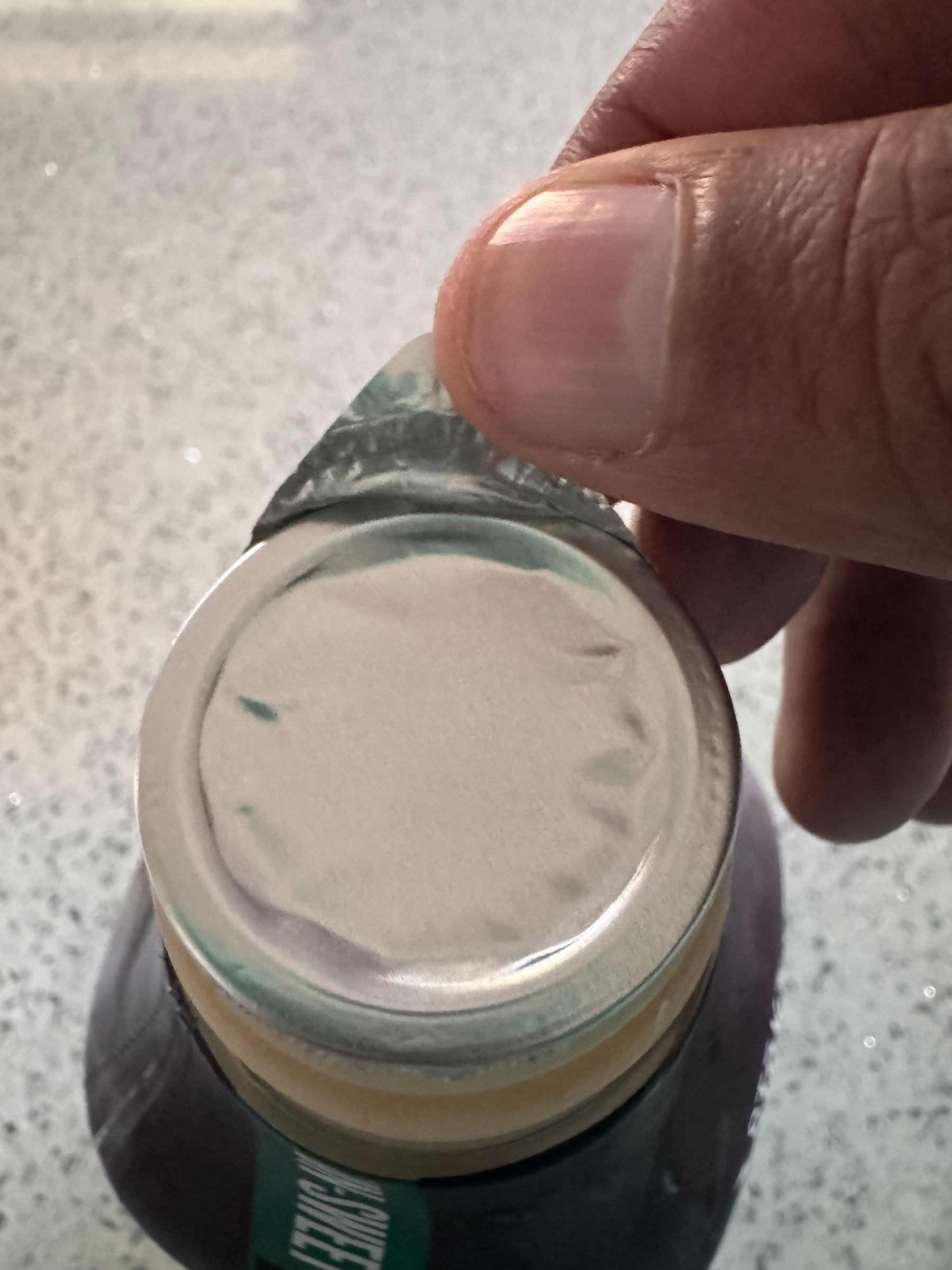 A hand is peeling back a foil seal from the top of a coffee container, revealing an unopened container.