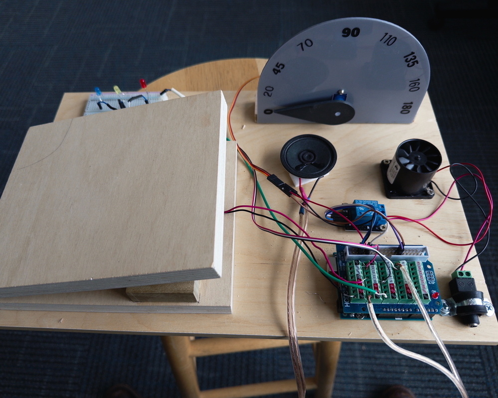 A homemade setup featuring electronic components including a breadboard, wires, sensors, and a dial, arranged on a wooden surface.