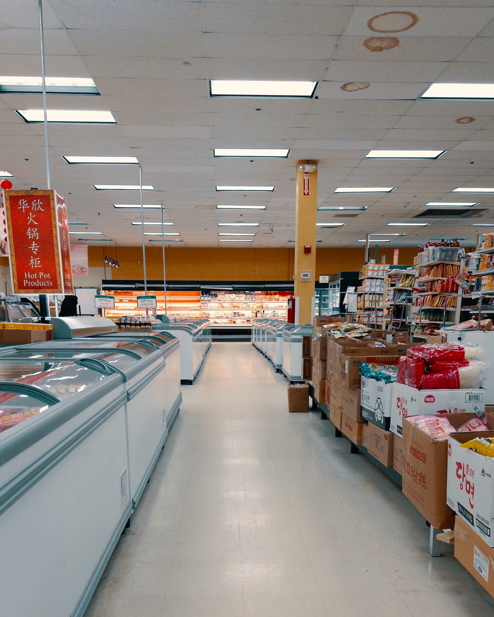 An aisle in a grocery store is lined with freezers on one side and shelves stocked with various products on the other.