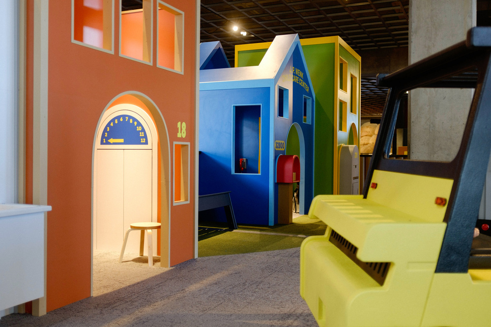 A colorful indoor play area features structures resembling houses and a vehicle-like play structure.