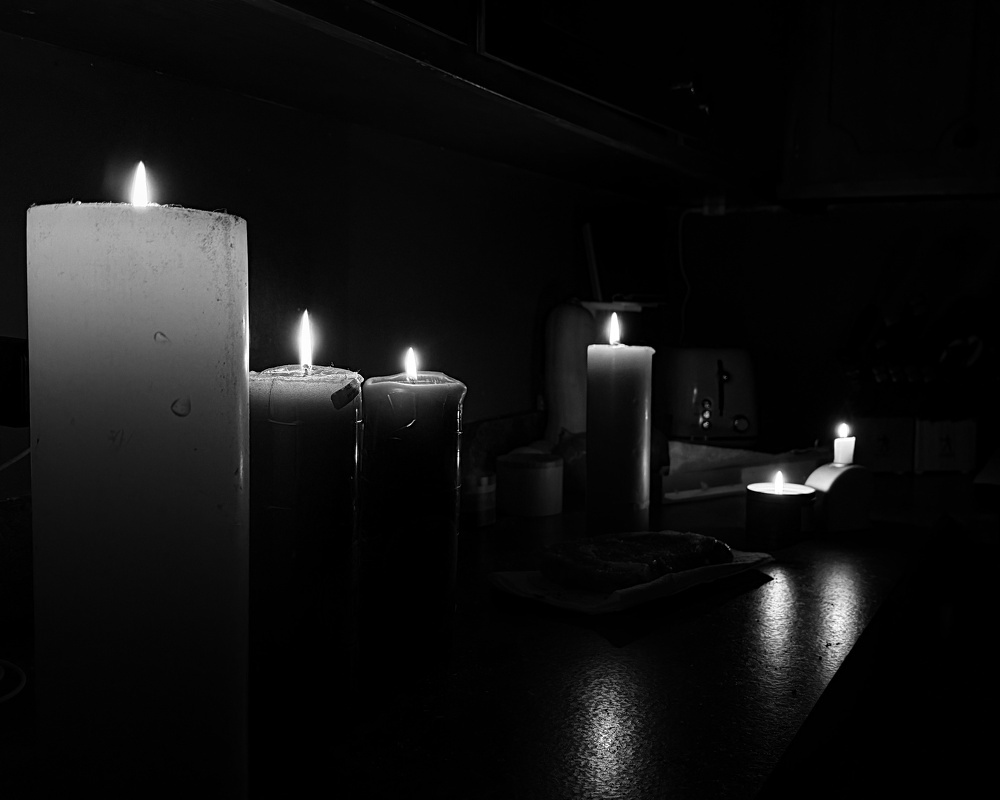 A row of lit candles illuminates a dark room, creating a serene and moody atmosphere.