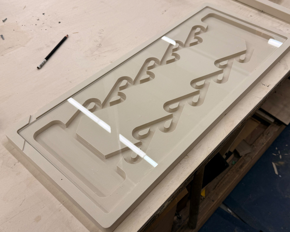 A wooden tabletop features a geometric cutout pattern with a pencil placed nearby.