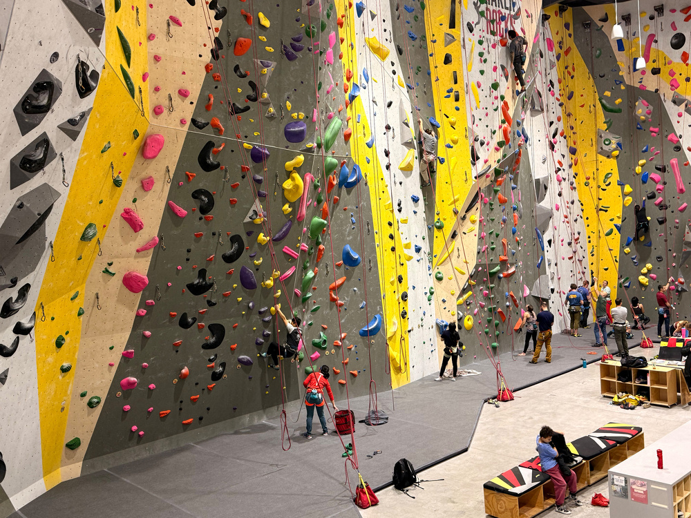 People are engaged in indoor rock climbing at a large gym with multicolored climbing walls and equipment.