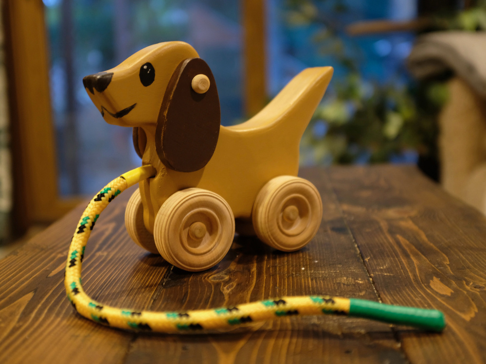 A wooden pull-toy in the shape of a dog with wheels and a yellow rope is placed on a wooden surface.