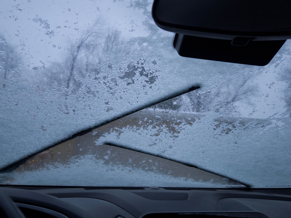 A car windshield is partially covered in frost or ice with wiper marks visible.
