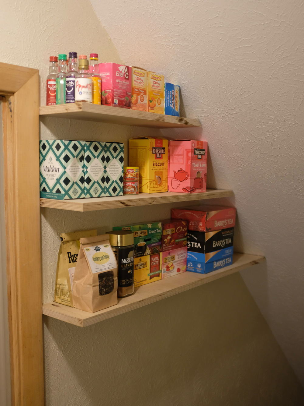 Wooden shelves filled with various packaged food items and beverages are mounted in a small corner space.