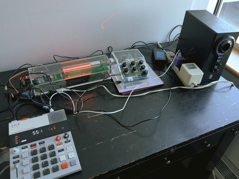 A setup featuring various electronic devices and cables, including a digital interface, a speaker, and a circuit board on a dark table.