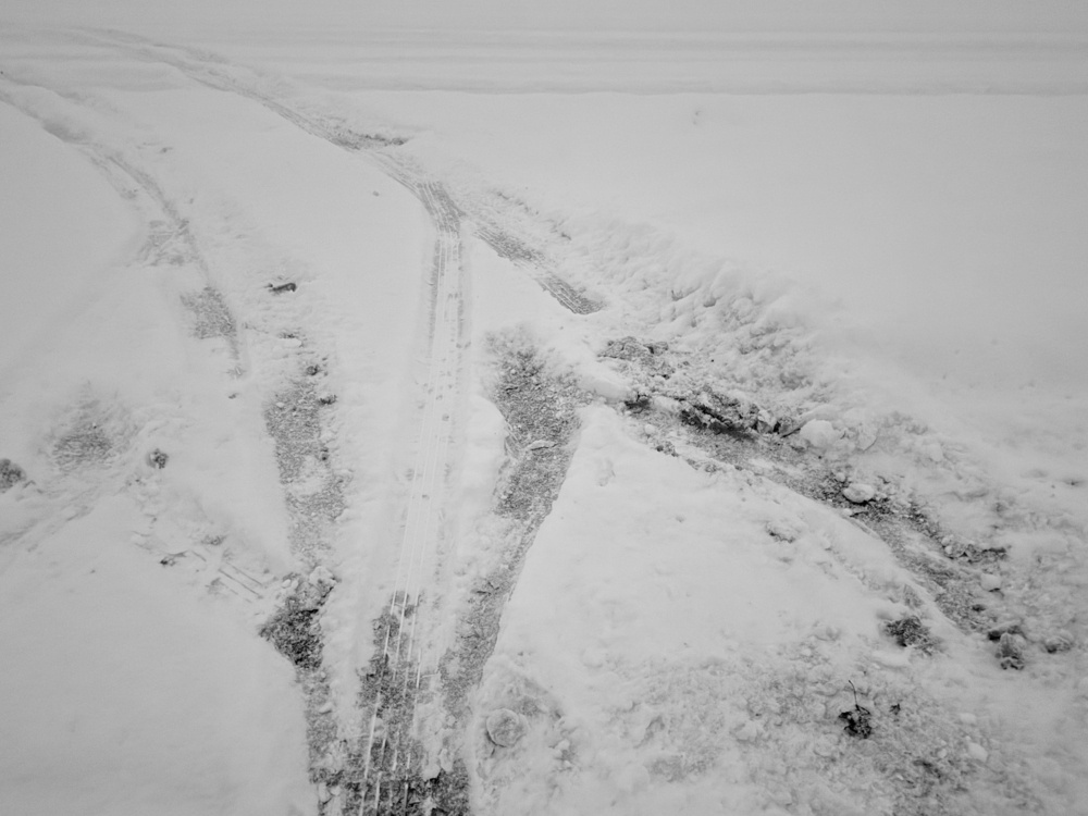 Tire tracks and disturbed snow create pathways through a snow-covered landscape.