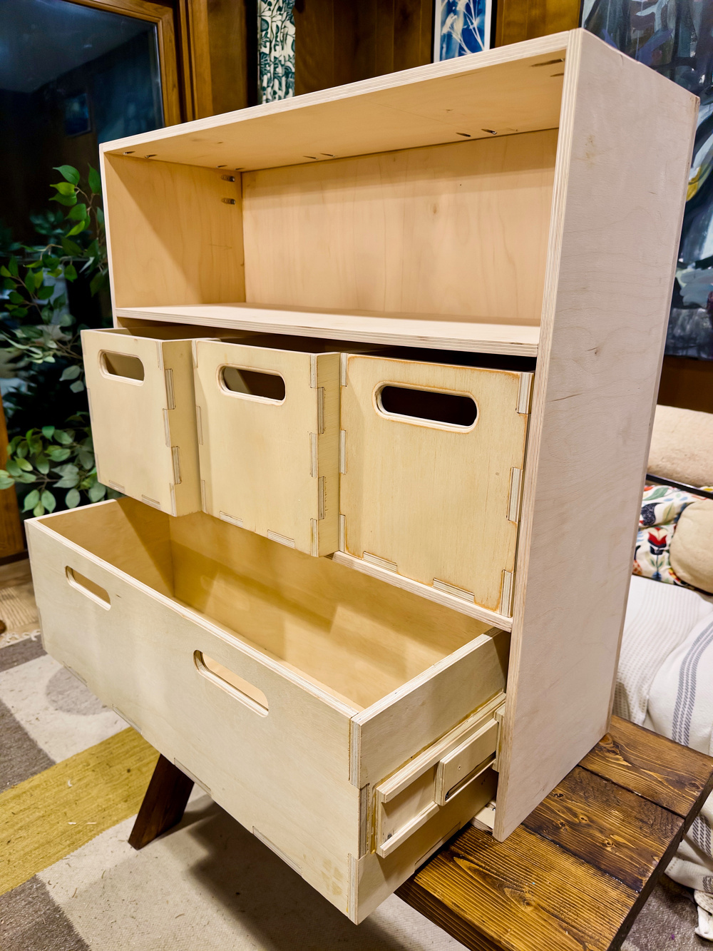 A wooden cabinet with open shelves, drawers, and cubbyholes is displayed in a room with a cozy aesthetic.