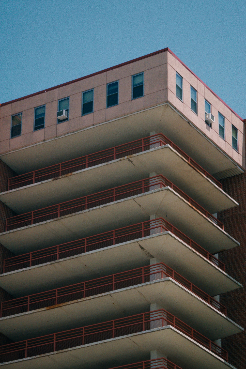 A multi-story building with balconies featuring red railings is set against a clear blue sky.