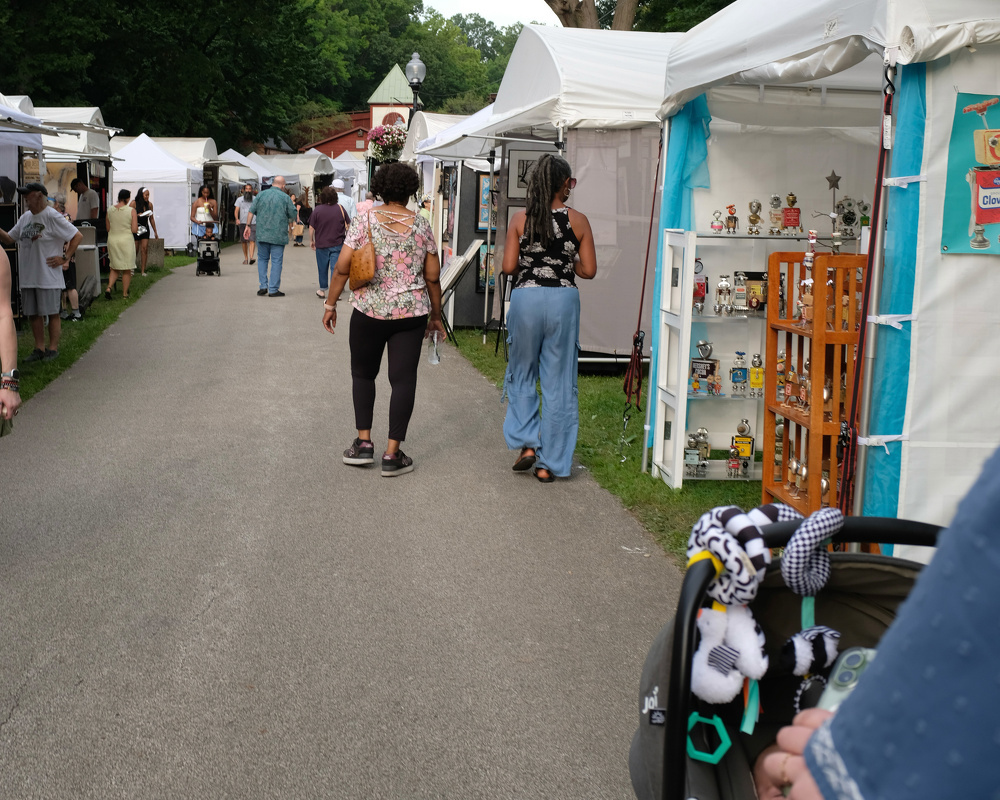 People are walking and browsing various booths at an outdoor art or craft fair.