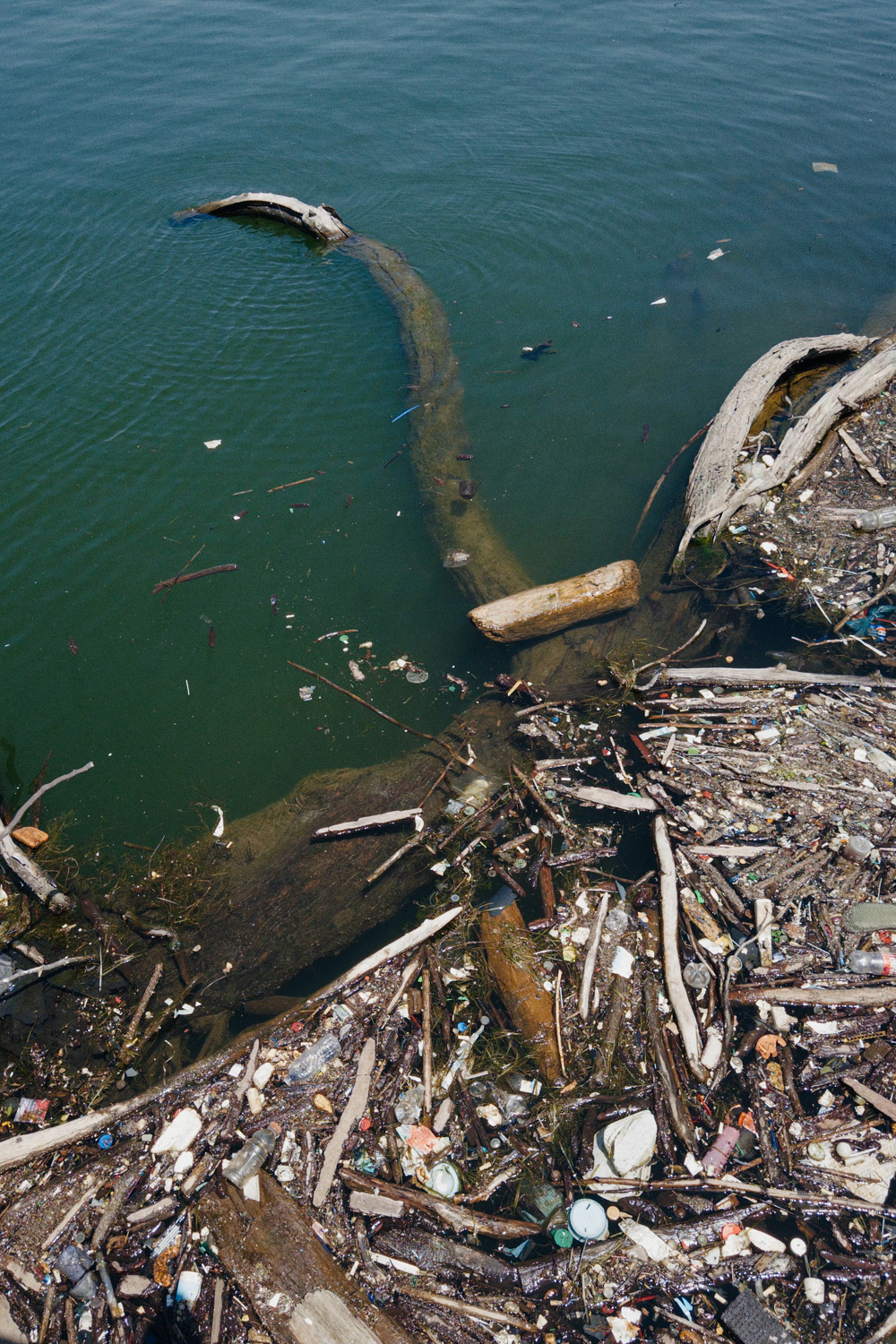 A water body is polluted with various types of debris and garbage, including wood, plastic, and other waste materials.
