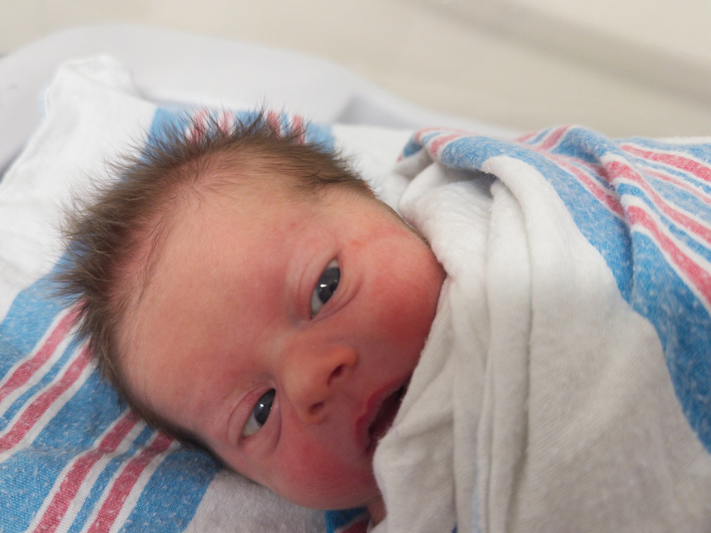 A newborn baby with spiky hair is wrapped in a white and blue-striped blanket.